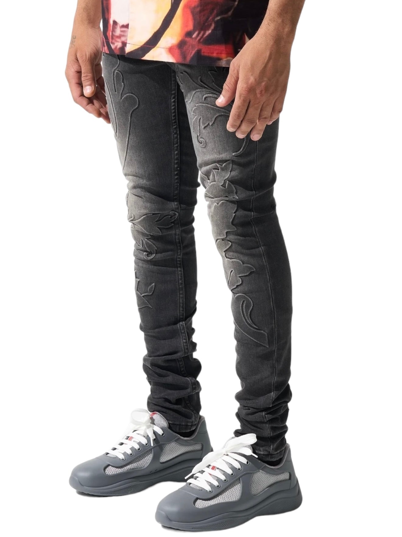 A man wearing black SERENEDE ROME JEANS BLACK, which feature an embroidered, skinny-fit design, paired with gray sneakers against a white background, photographed from waist to feet.