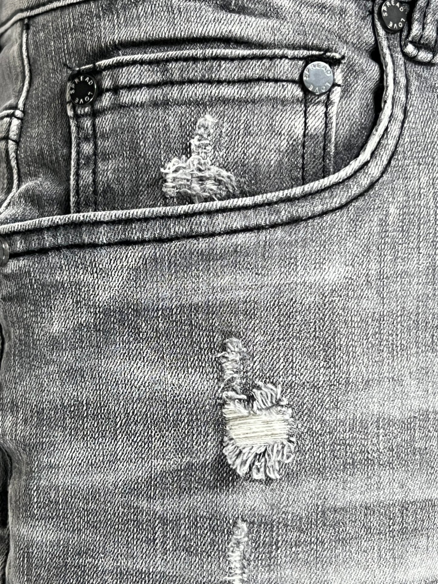 Close-up view of a faded SERENEDE TITAN JEANS GREY denim fabric with distressed details and riveted pockets.
