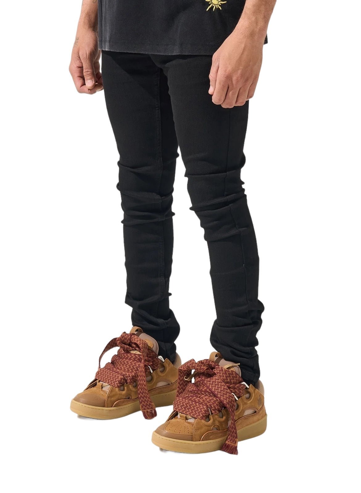 A person is wearing SERENEDE VANTA 11 JEANS BLACK, a black shirt, and brown sneakers with large, brown and red laces. Only the lower half of the body is visible.