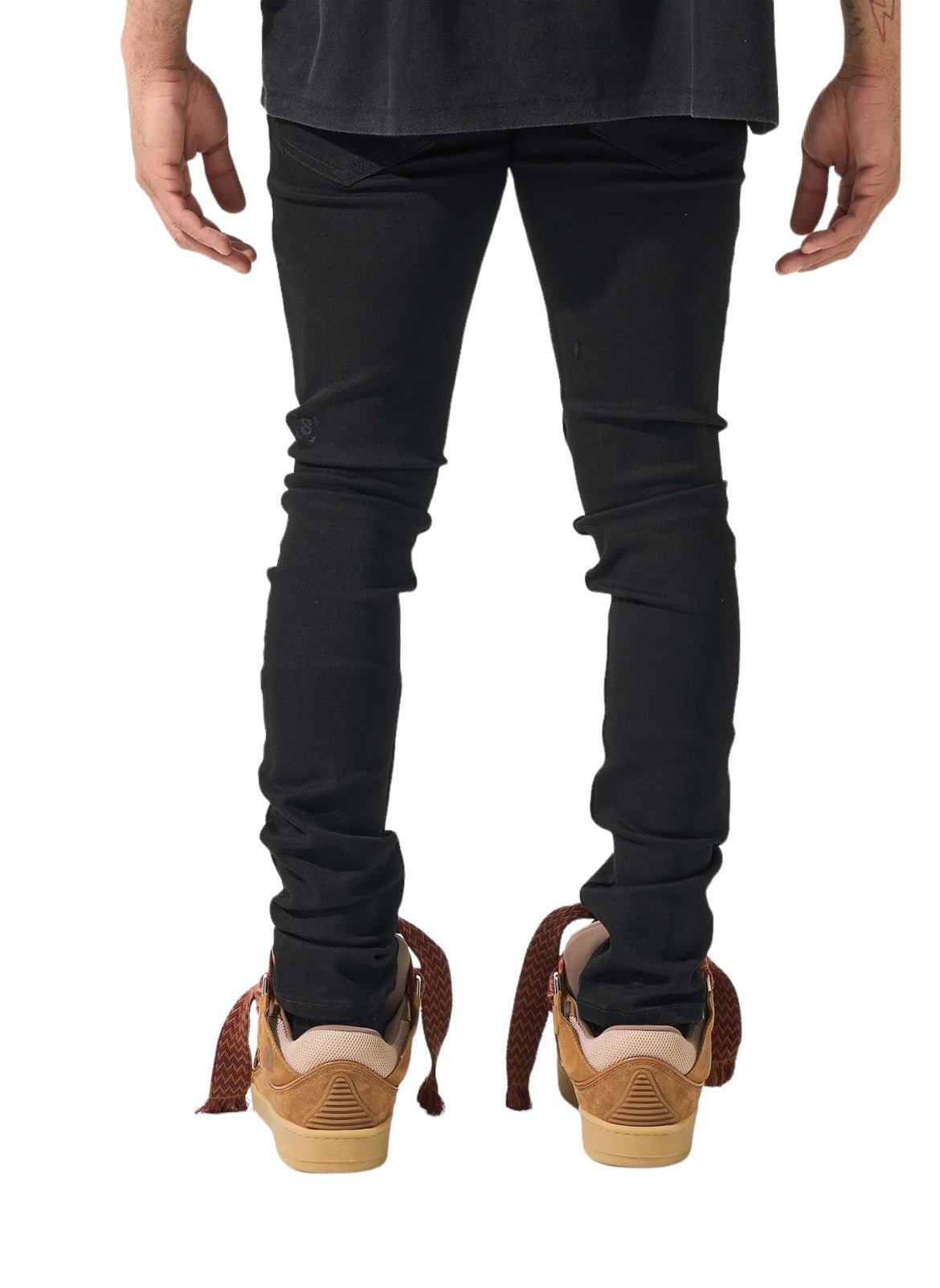 A person is standing with their back to the camera, wearing SERENEDE SERENEDE VANTA 11 JEANS BLACK made from premium fabric, a black shirt, and brown sneakers with decorative elements.