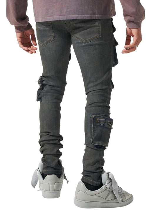 A person wearing SERENEDE WAVE CARGO JEANS in Atlantic dark blue with patchwork pockets and white sneakers stands with their back to the camera.