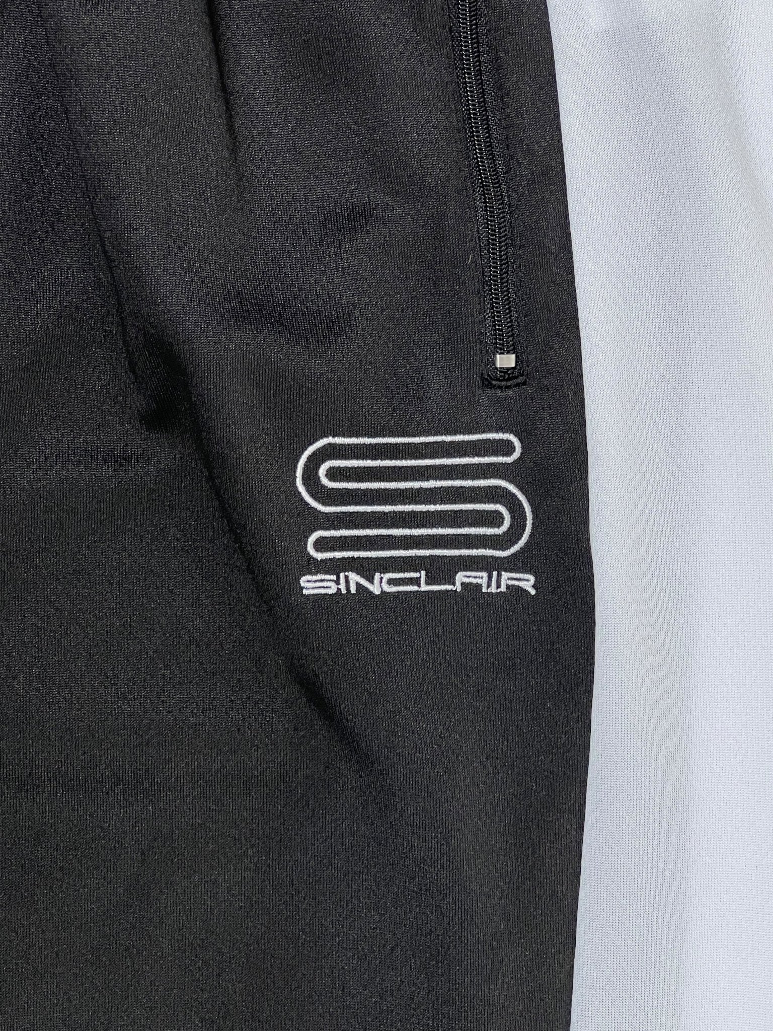 Close-up of black fabric showcasing the SINCLAIR brand's signature white embroidered 'S' logo and "SINCLAIR" text, echoing the refined style of Sinclair SMB65 Tech Logo Track Pant Black.