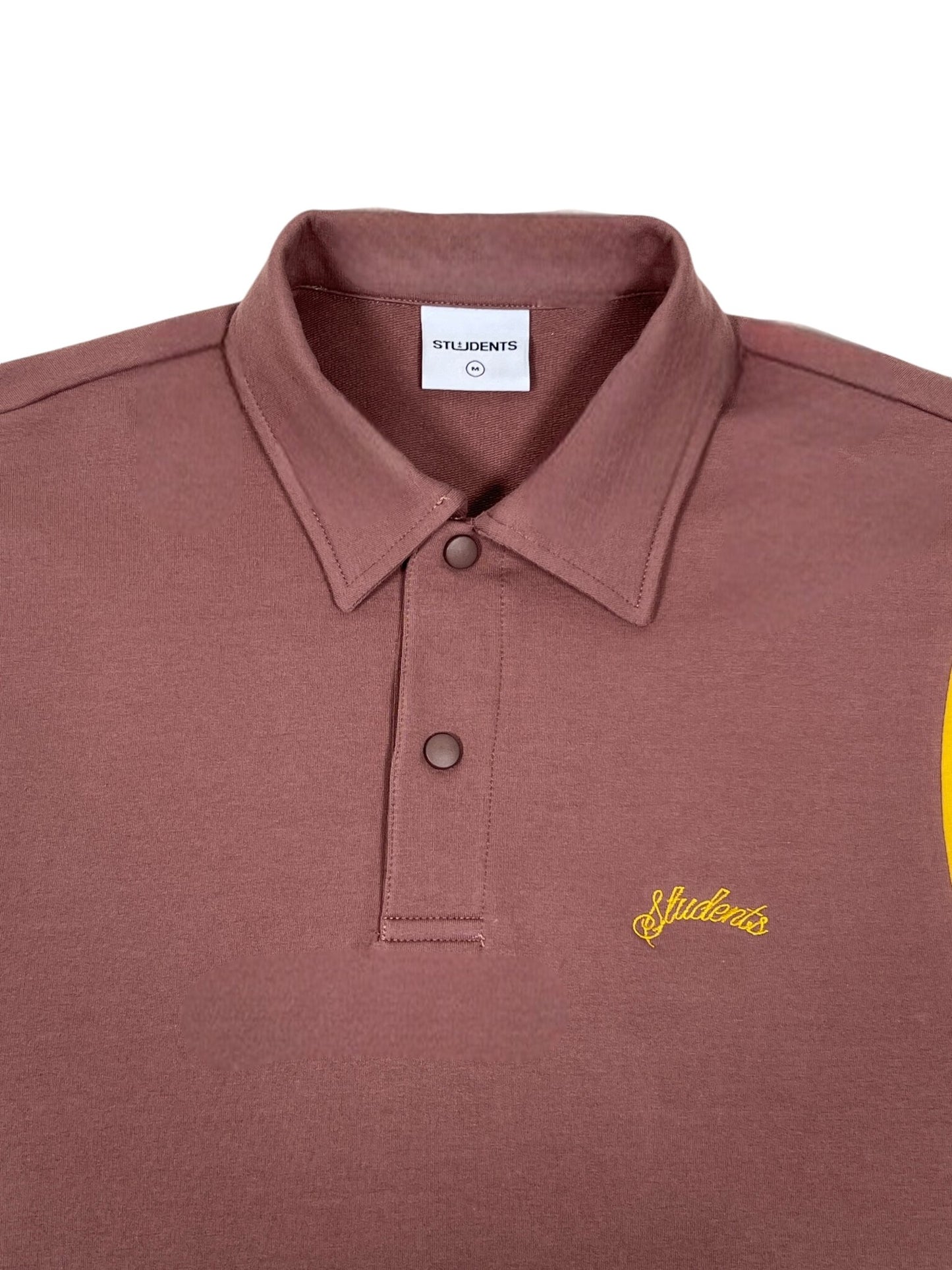 The Callum long-sleeve polo shirt in brown, designed by STUDENTS, features a buttoned collar and is made from soft French terry cotton. The word "Students" is embroidered in yellow on the front.