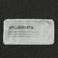 Close-up of a fabric label on the "Students Estudiantes Pullover Hood Blk" by STUDENTS with a motivational message, sewn onto 100% cotton black hoodie material.