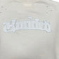 The Untitled Artworks Crewneck Short Sleeve Cream by UNTITLED ARTWORKS is a 100% cotton cream sweatshirt with "Hooded" stitched across the back in a distressed, gothic-style font.
