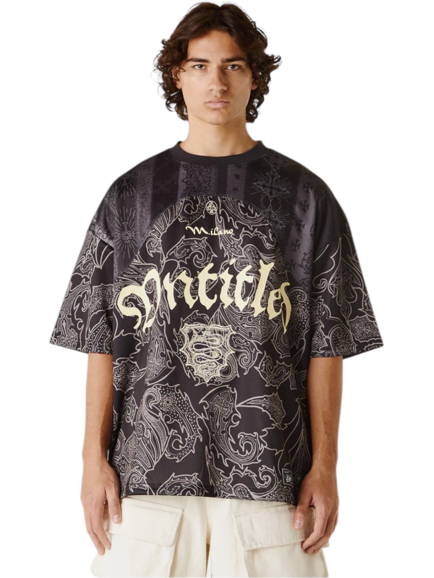 A person wears the UNTITLED ARTWORKS Untitled Artworks Sport Jersey Tee Black, featuring white abstract patterns and gold gothic-style text, paired with light pants, standing against a white background.