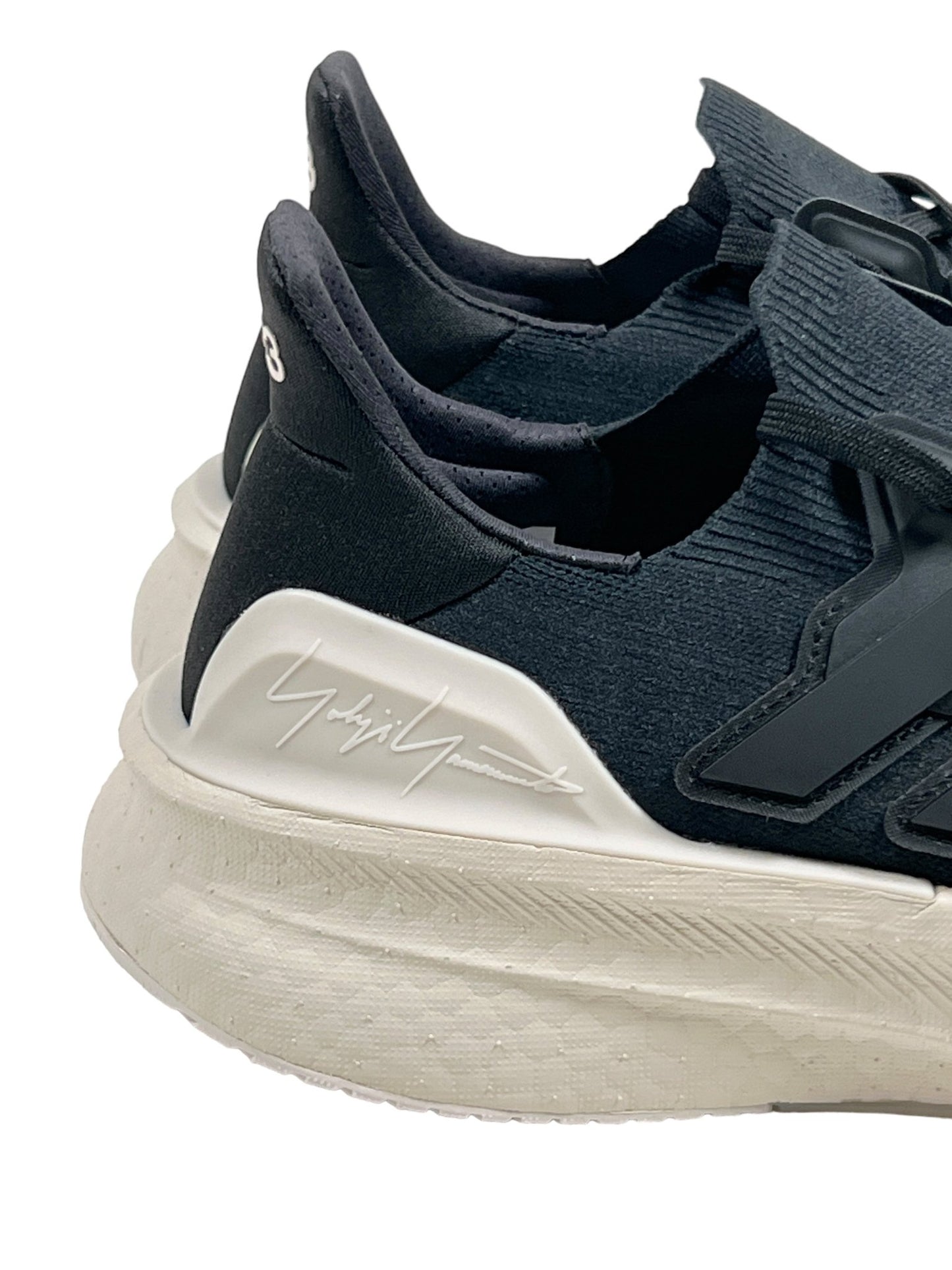 Close-up of a pair of black and white ADIDAS x Y-3's Y-3 IH0871 Ultraboost 5 Cblack/Alum sneakers with a signature on the side, featuring a textured white sole and sleek adidas PRIMEKNIT design.