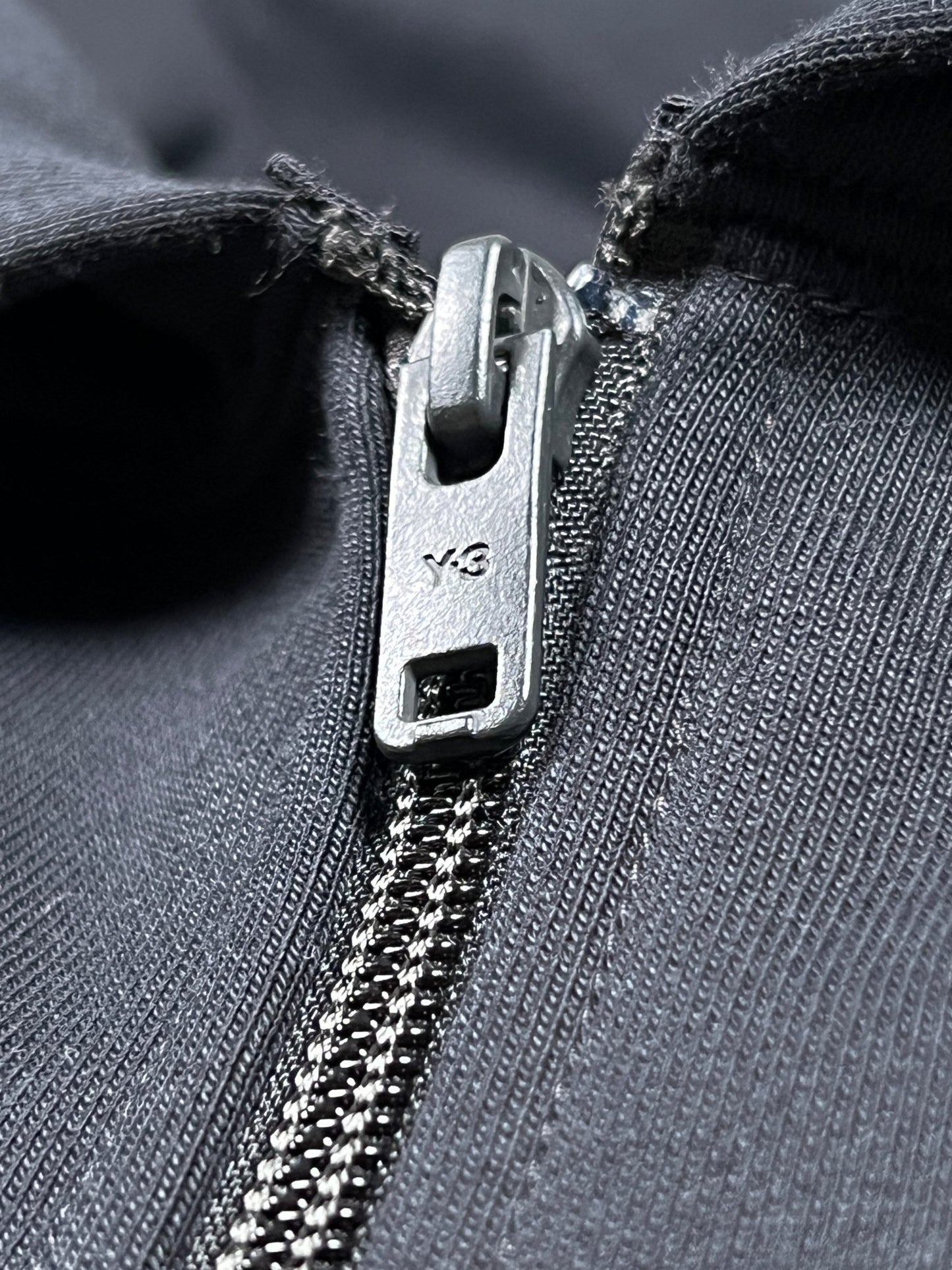 Close-up of a partially zipped black YKK zipper on dark fabric, revealing the sleek elegance characteristic of an ADIDAS x Y-3 JE9278 Logo Zip Hoodie in black.