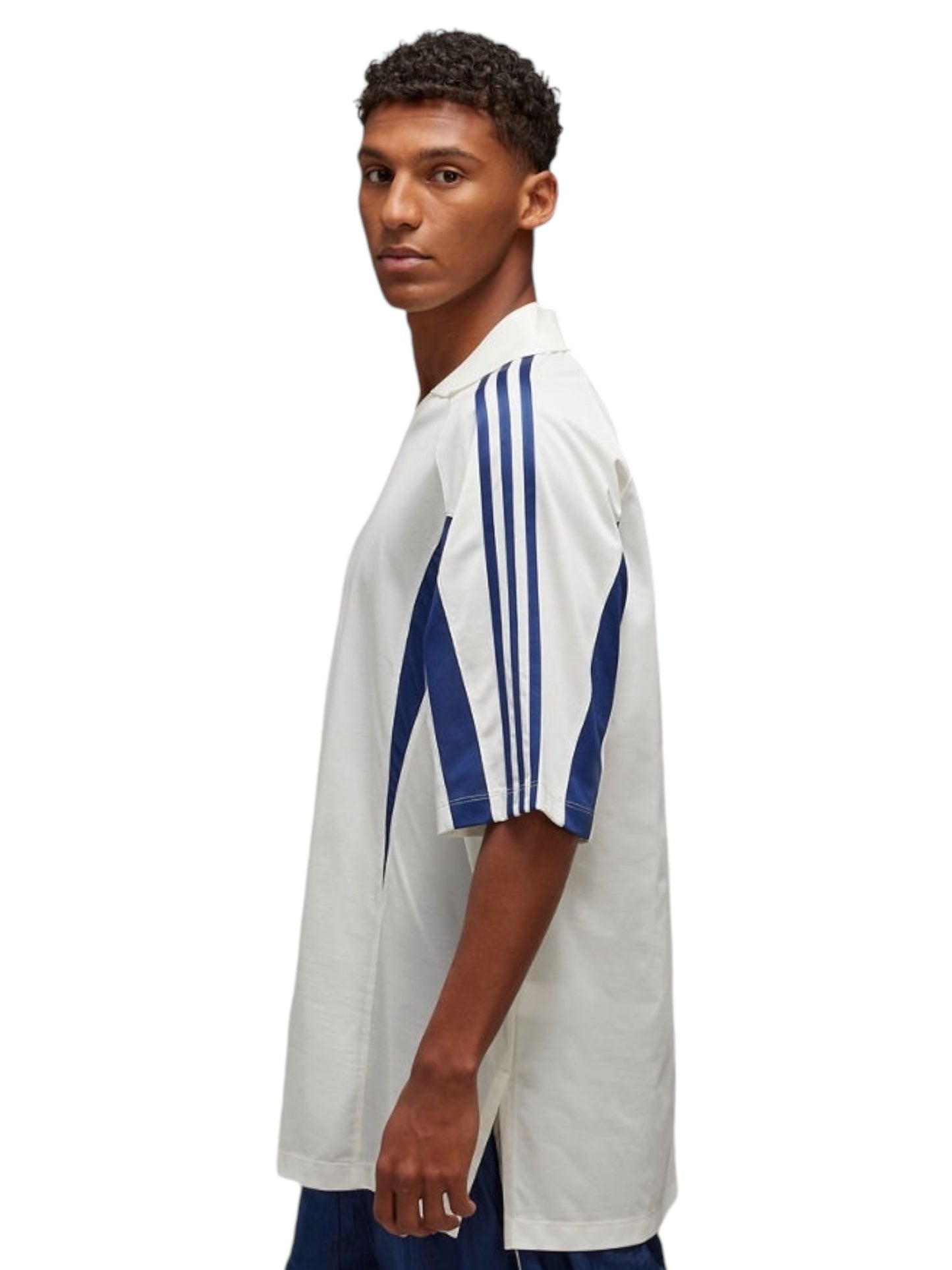 A young man in a Y-3 JM3222 SS CTLN Tee Cwhite, featuring blue stripes inspired by ADIDAS x Y-3, looks over his shoulder against a pristine white background.