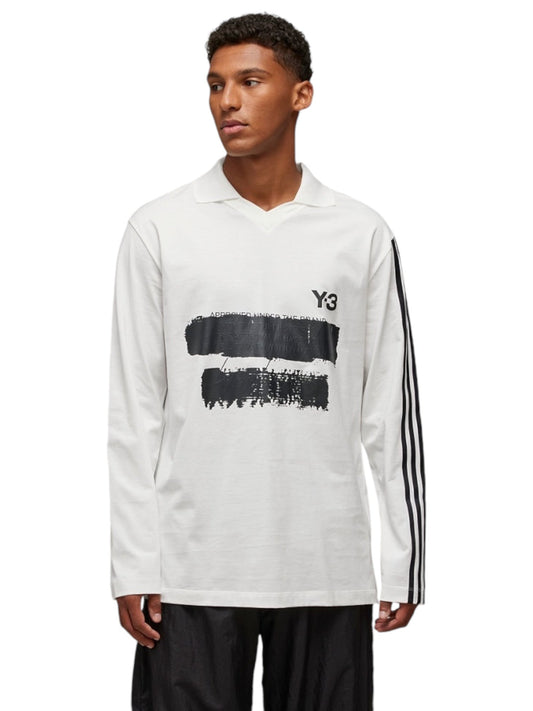 A person is showcasing a sophisticated look in the Y-3 JM3233 U GFX Logo LS T Cwhite by ADIDAS x Y-3, featuring a crisp white long-sleeve design with a striking black graphic and the iconic Y-3 logo, along with three black stripes on the sleeve. This fashionable top complements sleek black pants beautifully, providing a refined appearance suitable for any occasion.