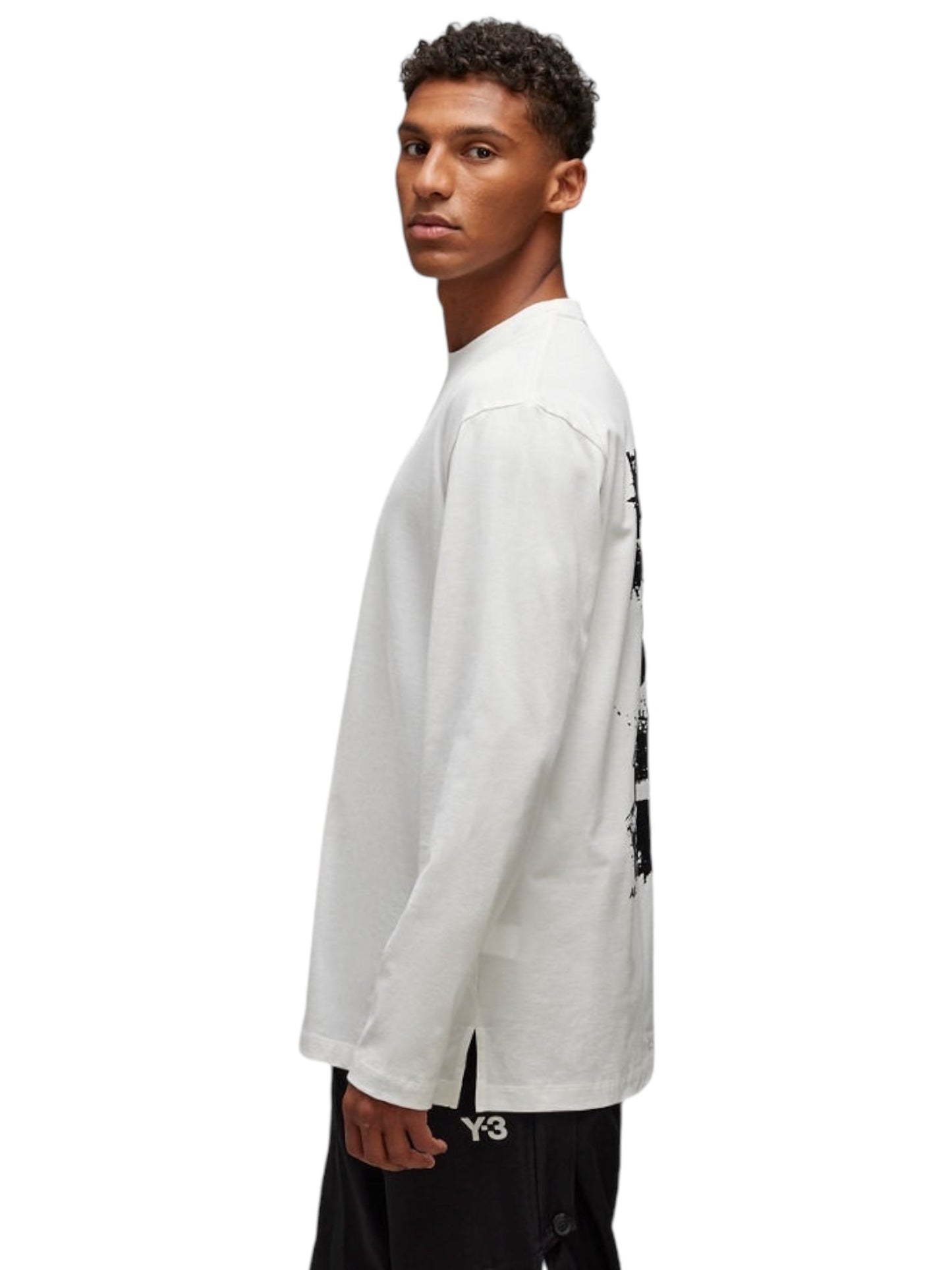 A person wearing the ADIDAS x Y-3 JM3234 U GFX LS Tee Cwhite, a white long-sleeve tee made from soft cotton and displaying text on the back, is paired with black shorts while standing sideways against a pristine white background.