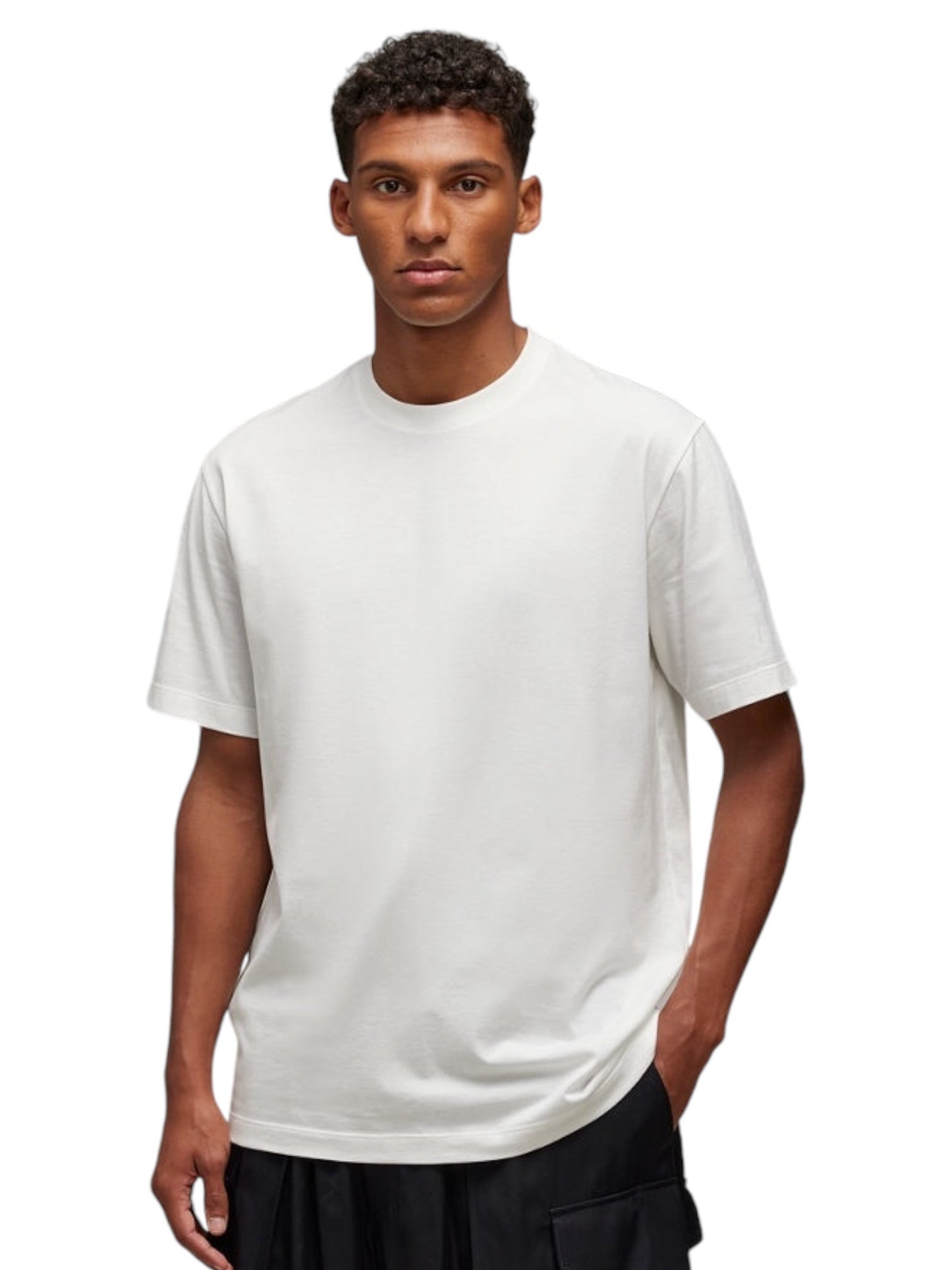 A person in a Y-3 JM7815 U GFX SS Tee Cwhite stands against a white background, hands in pockets, looking forward, showcasing ADIDAS x Y-3 designs crafted from soft cotton fabric.