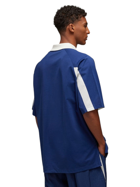 A person wearing the Y-3 JM8338 SS CTLN Tee in dark blue and white, made from cotton and polyester by ADIDAS x Y-3, stands with their hands in their pockets, viewed from the side.