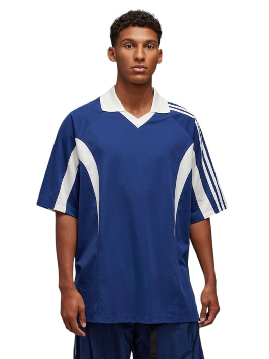 A person stands against a white background, wearing the Y-3 JM8338 SS CTLN Tee Dkblue, featuring blue and white vertical stripes on the sleeves. This Adidas x Y-3 jersey showcases the logo prominently and combines cotton and polyester for ultimate comfort.