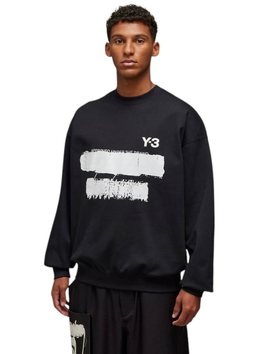 A person styled in fashionable classics wears a black ADIDAS x Y-3 JN4881 U GFX Crew sweatshirt, made from a cotton-polyester blend with a white graphic design, paired with black pants on a white background.