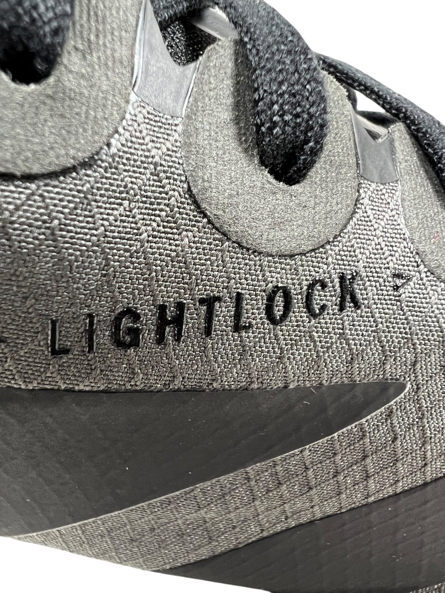 Close-up of a Y-3 JS3155 Y-3 Adios Pro 4 M sneaker by ADIDAS x Y-3 in Cinder/Black, featuring textured fabric and "LIGHTLOCK" embossed on the side. Black laces are visible, along with the iconic 3-Stripes logo subtly enhancing its sleek design.