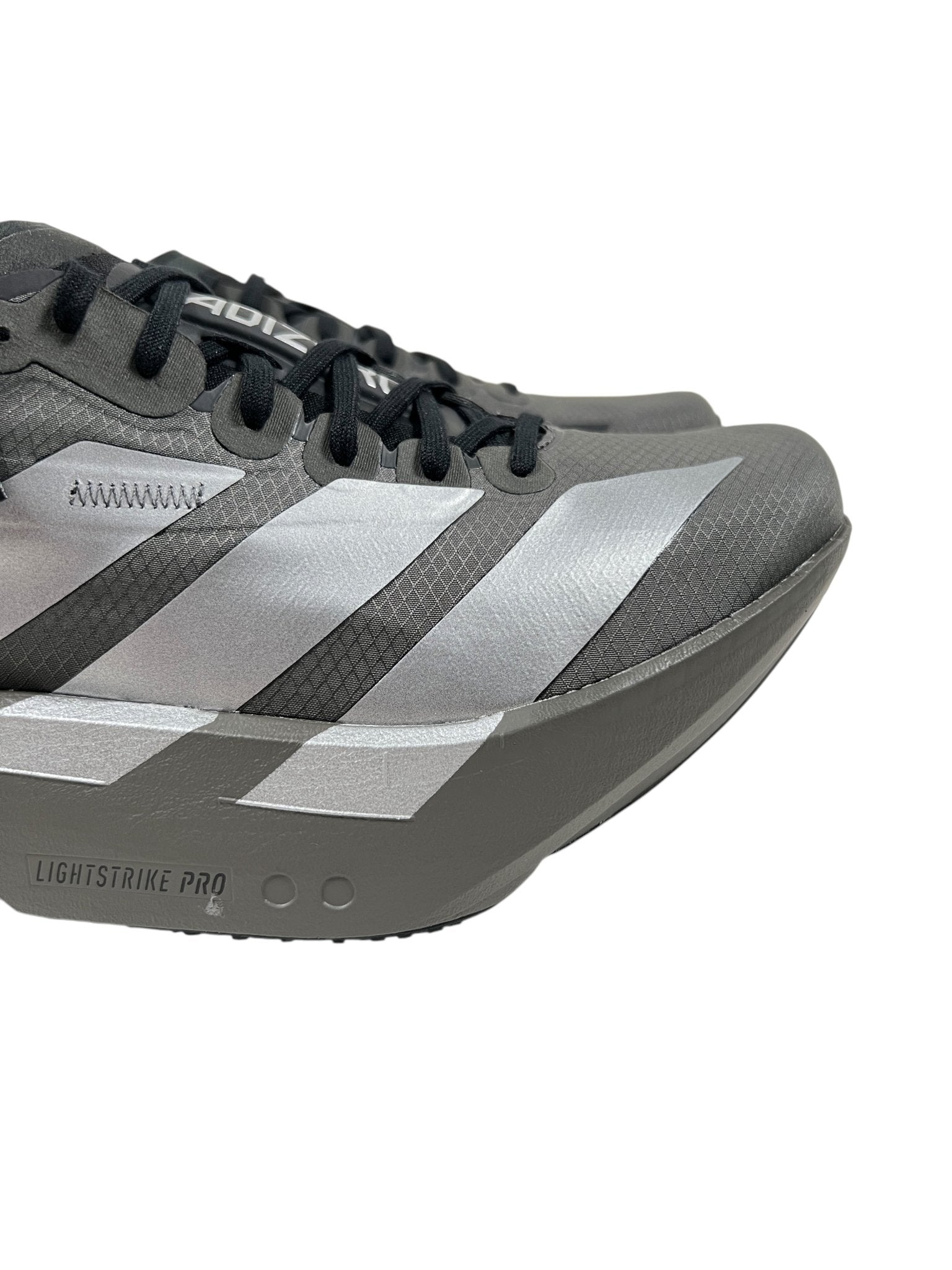 Close-up of a Y-3 JS3155 Adios Pro 4 M sneaker in Cinder/Black by ADIDAS x Y-3, showcasing a textured gray and silver surface with the iconic 3-Stripes logo, black laces, and a thick sole marked "Lightstrike Pro.