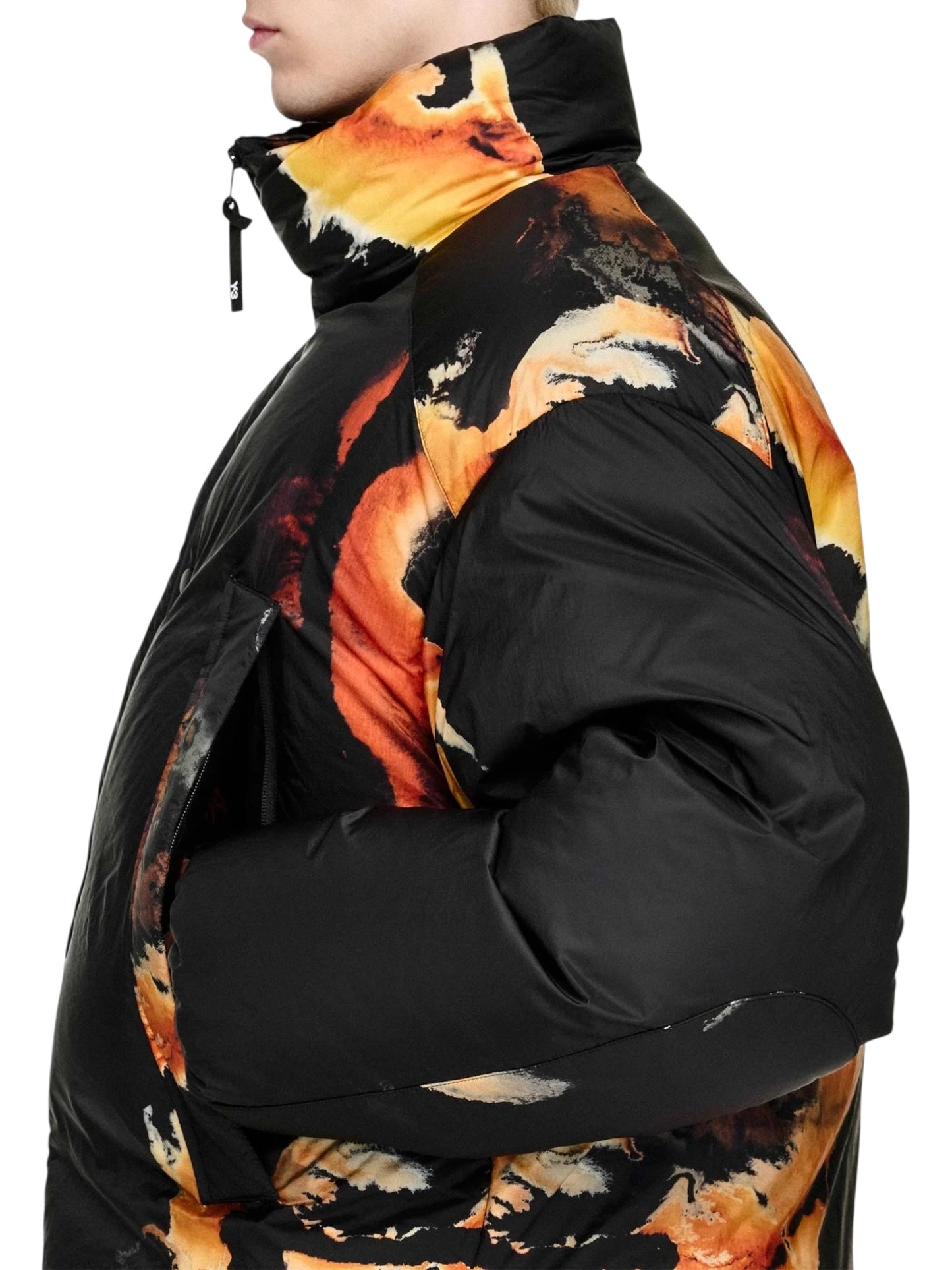 A person in the ADIDAS x Y-3 KA2364 M AOP Puff JKT Multco/Black, a black polyamide puffer jacket with an orange and yellow abstract pattern, is photographed from the side.