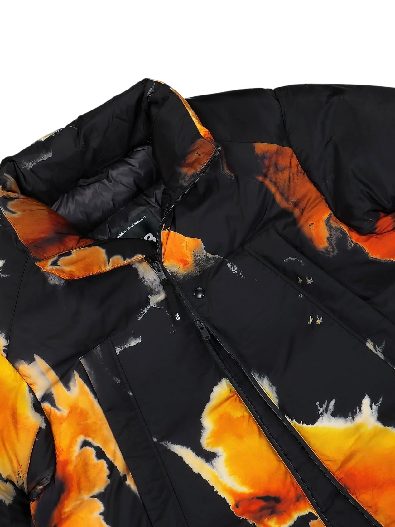 Close-up of the ADIDAS x Y-3 KA2364 M AOP Puff JKT Multco/Black, a puffer jacket with bold orange and yellow abstract patterns on black, PrimaLoft insulation, high collar, and zipper closure.