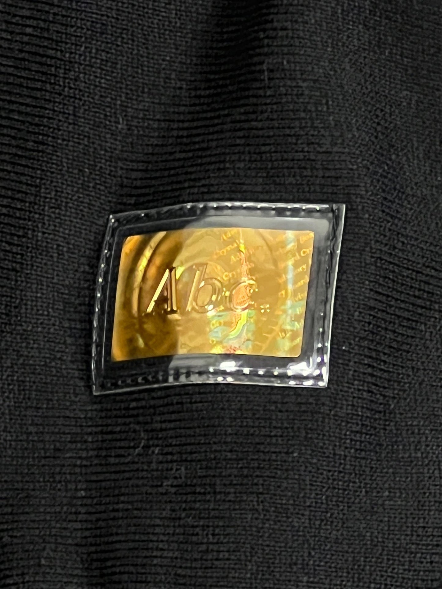 A close up of a gold label on an ADVISORY BOARD CRYSTALS TRI-TONE CREWNECK SWEAT ANTHRACITE BLK sweatshirt.