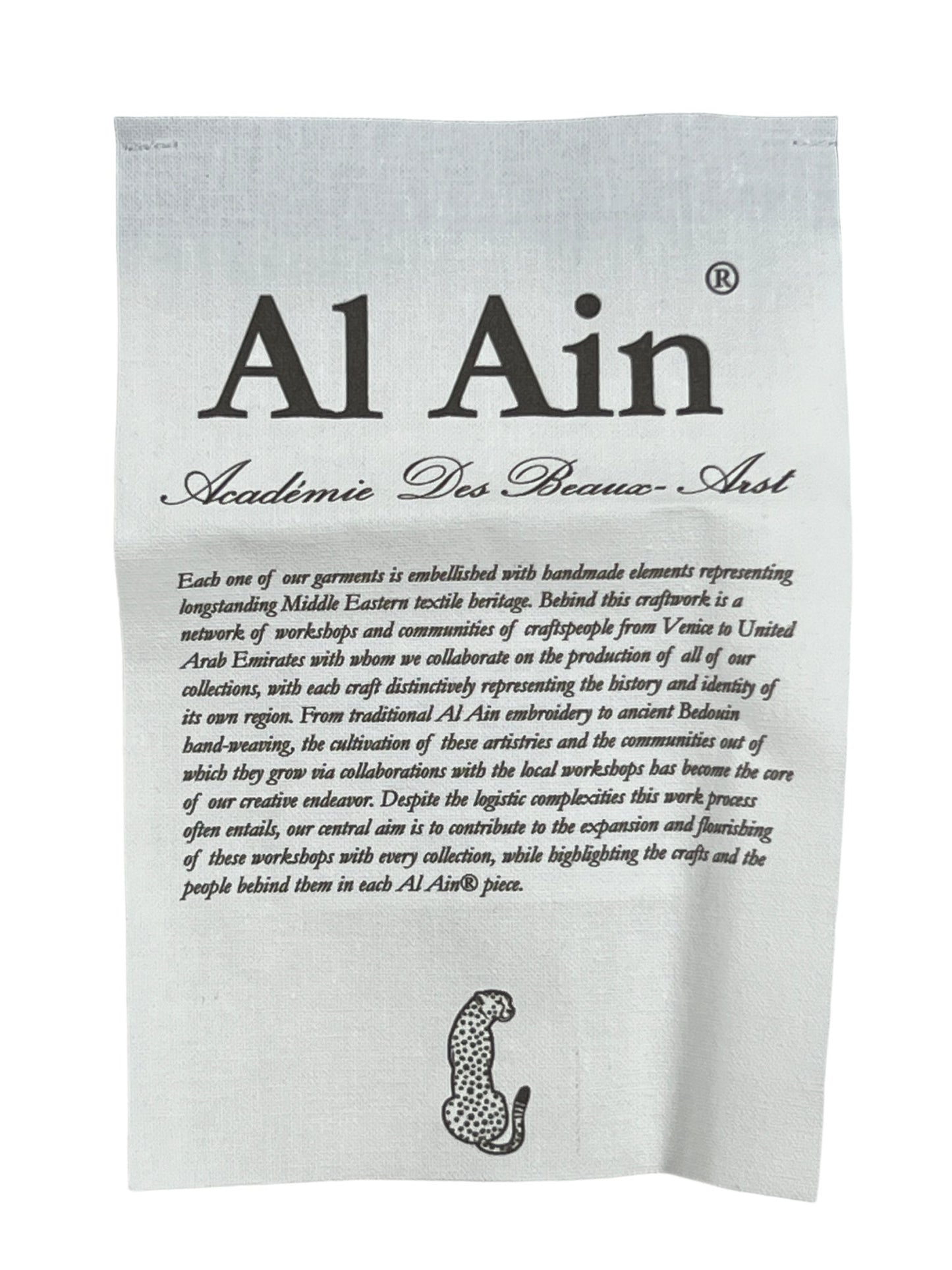A fabric label for "AL AIN AHOX S102 PALMIER CHAMEAU" with elegant text and an academic emblem, describing the brand's commitment to beauty and artisanship in the creation of their streetwear look products.