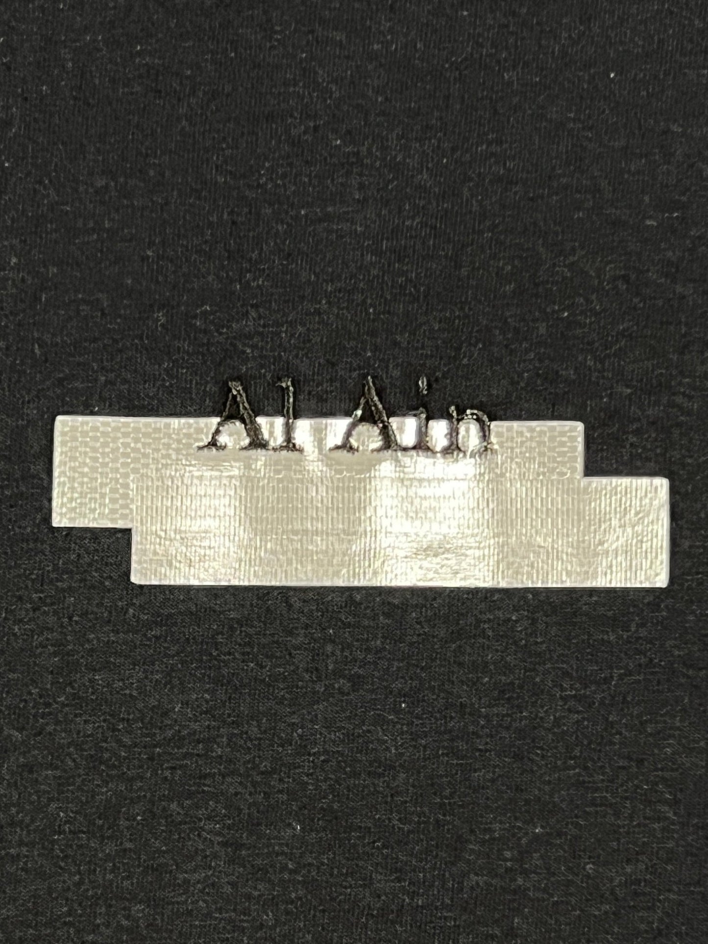 A piece of AL AIN AMHX S120 JABALIA NOIR duct tape with staples on it against a black background.