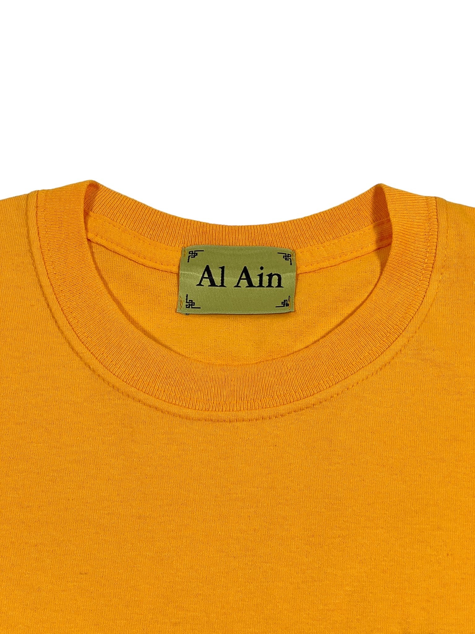 Close-up of the neckline of the Al Ain AMHX S120 Jabalia Ocre Yellow t-shirt, featuring a green AL AIN label.