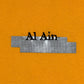 The AL AIN "Al Ain AMHX S120 Jabalia Ocre Yellow" features the text "Al Ain" partially covered by two overlapping silver duct tape strips on an ochre yellow background, creating a bold, graphic T-shirt-inspired detail.