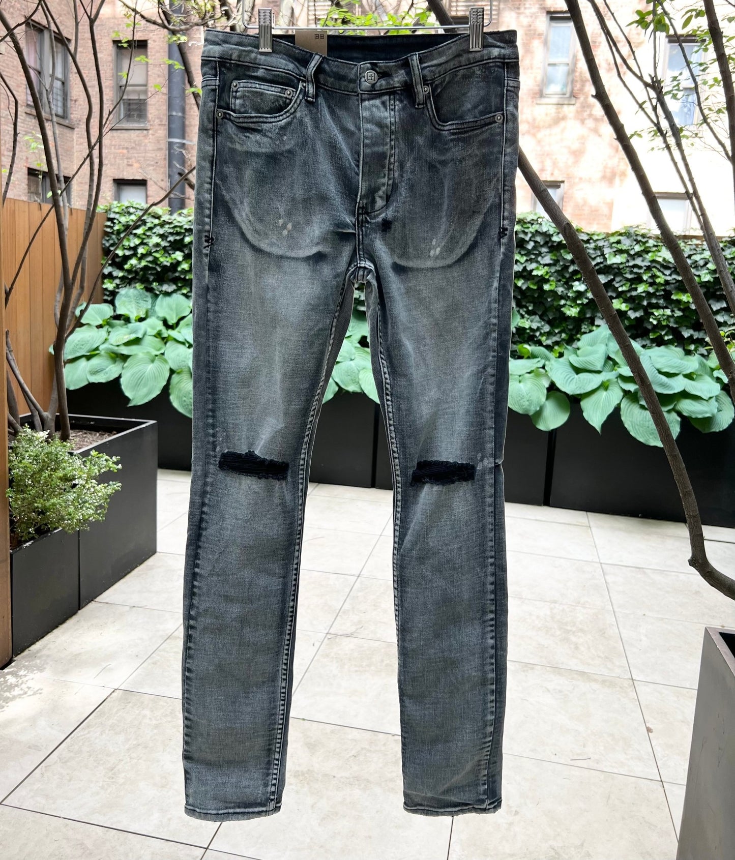 A pair of men's Ksubi CHITCH HYPNOTIZE TRASHED DENIM jeans, model MPF22DJ016, hanging on a hanger in front of a tree.