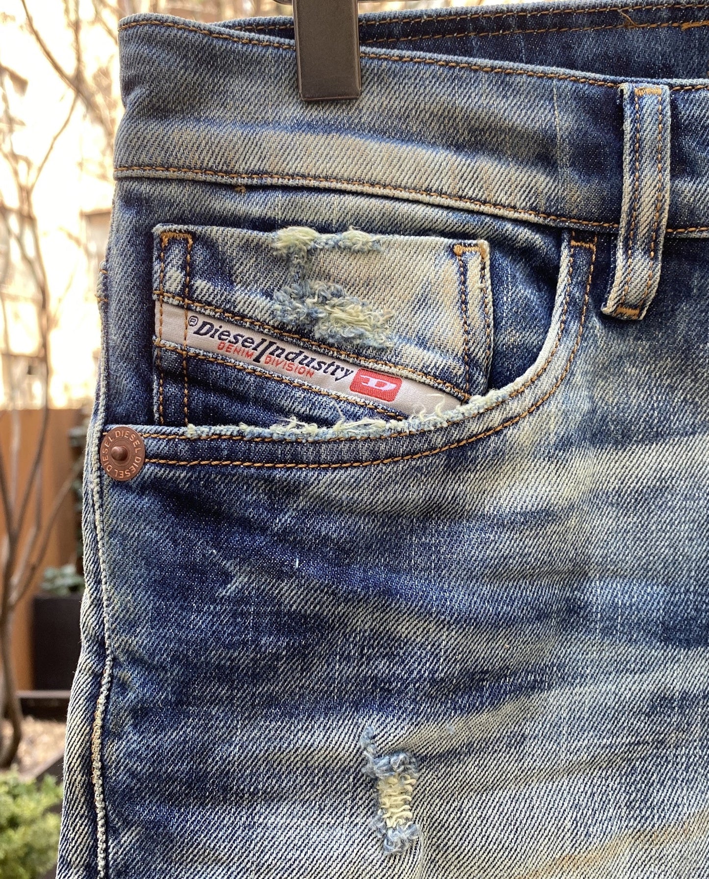 A pair of faded, distressed jeans hanging on a DIESEL D-KRAS-X-SP4 09VI DENIM hanger.