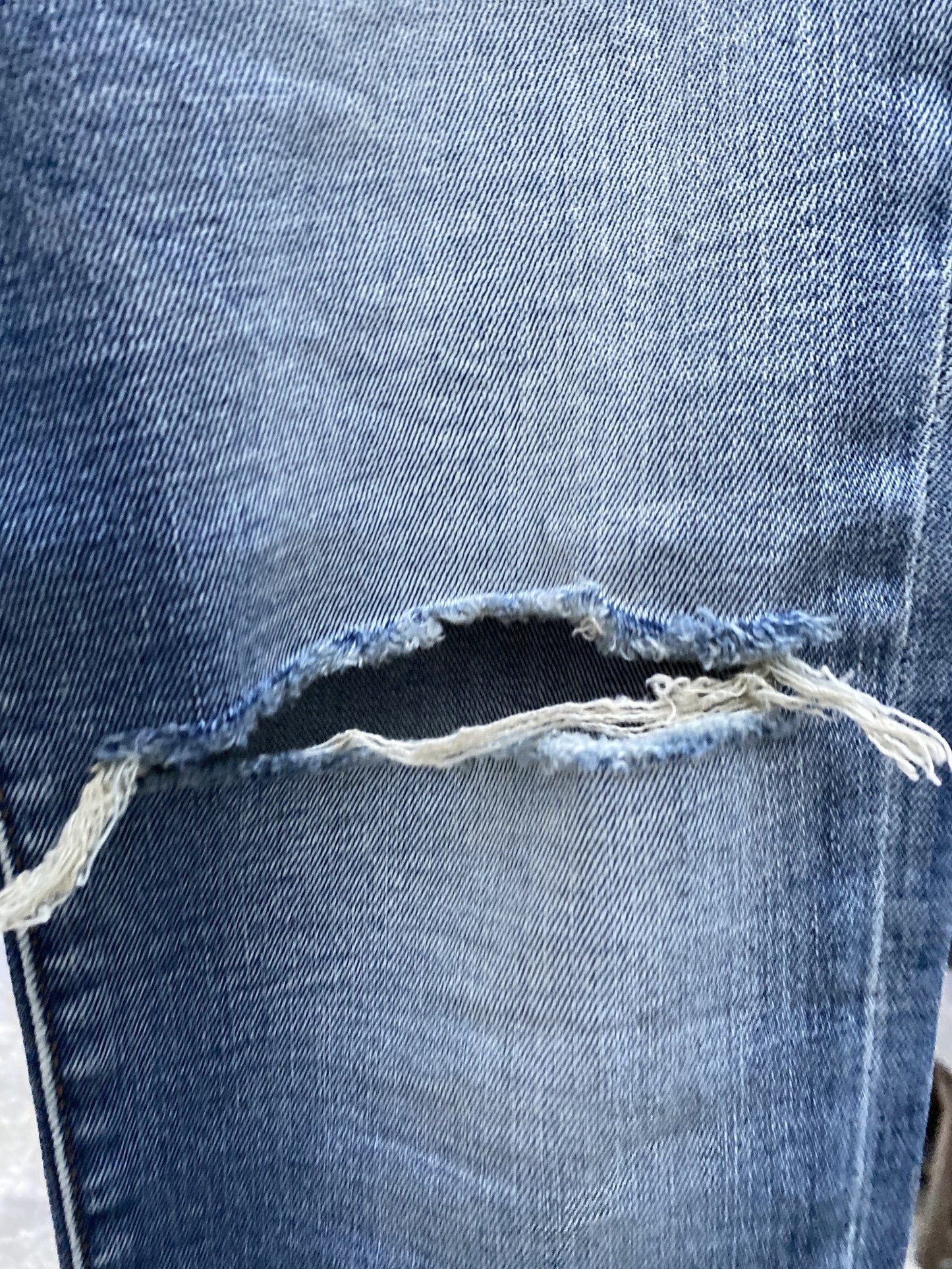 A close up of a pair of light blue DIESEL D-STRUKT 9C87 DENIM ripped jeans with holes in them.