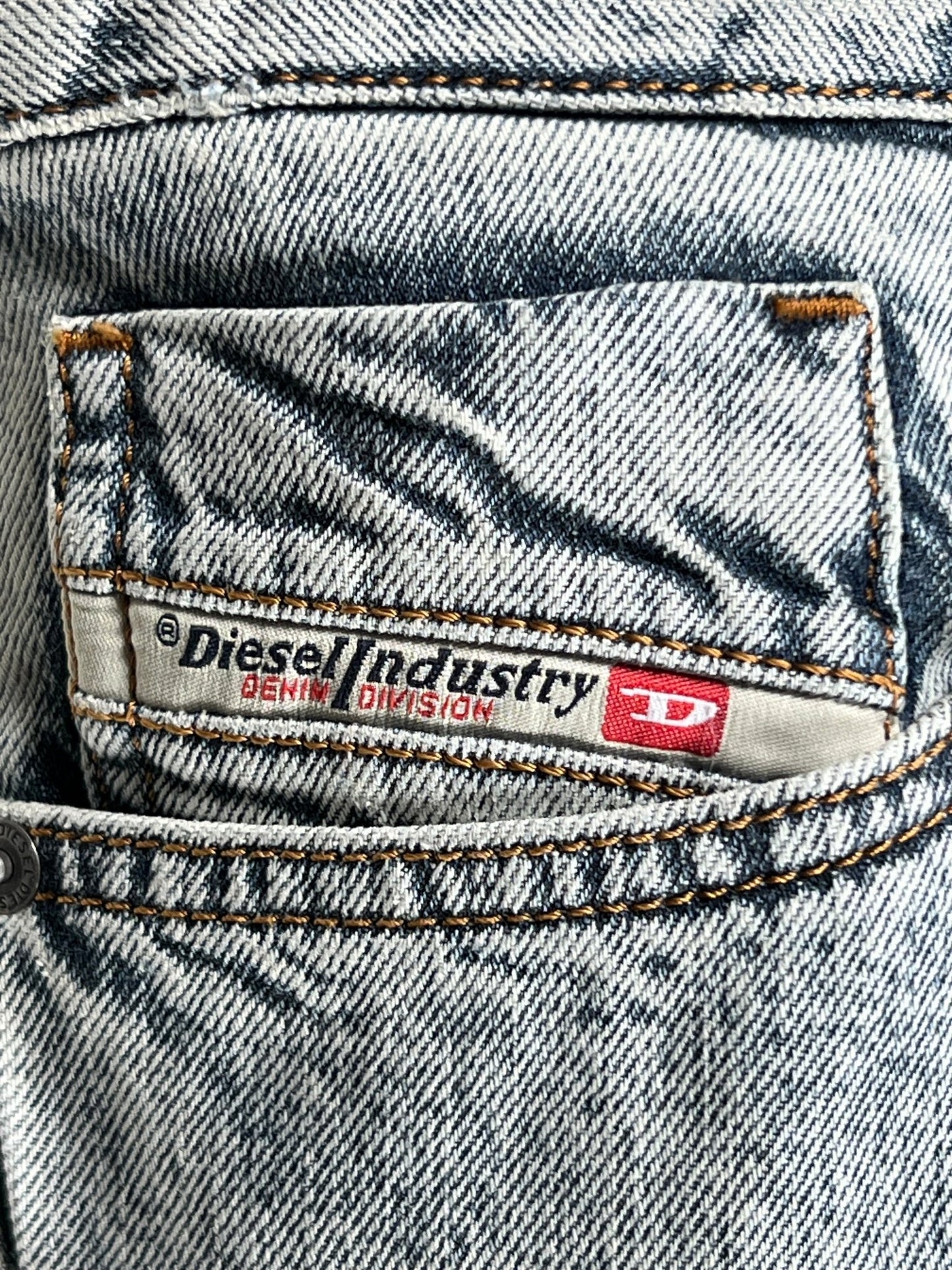 A label on a piece of denim clothing reading "DIESEL 1955 D-REKIV-S1 9160 DENIM industry denim division" with orange stitching details.