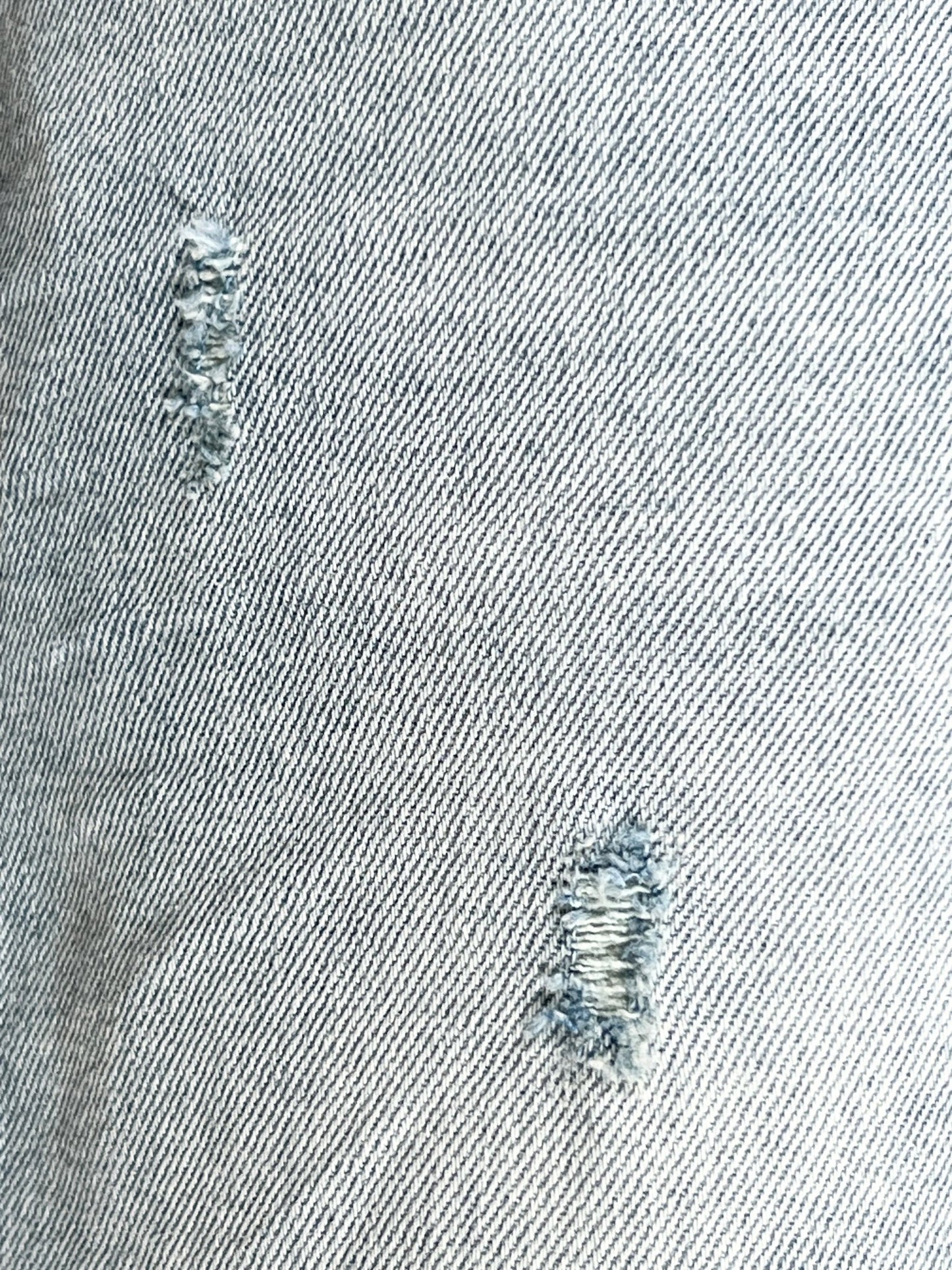 Close-up of a distressed DIESEL stretch denim fabric with frayed holes.