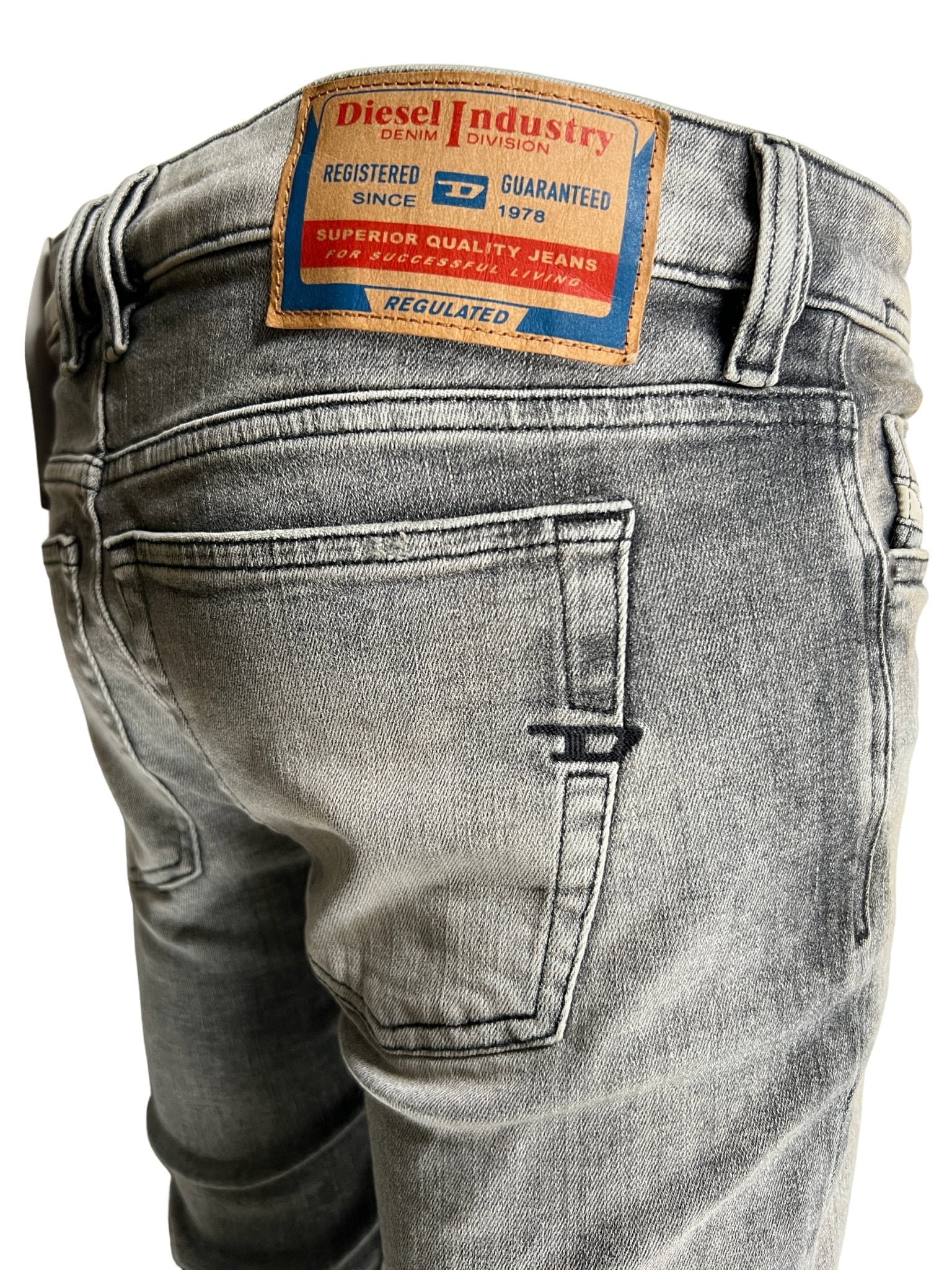 Close-up of Diesel 1979 Sleenker 9H74 light gray skinny jeans made from stretch denim, with a DIESEL Industry label on the back waistband.