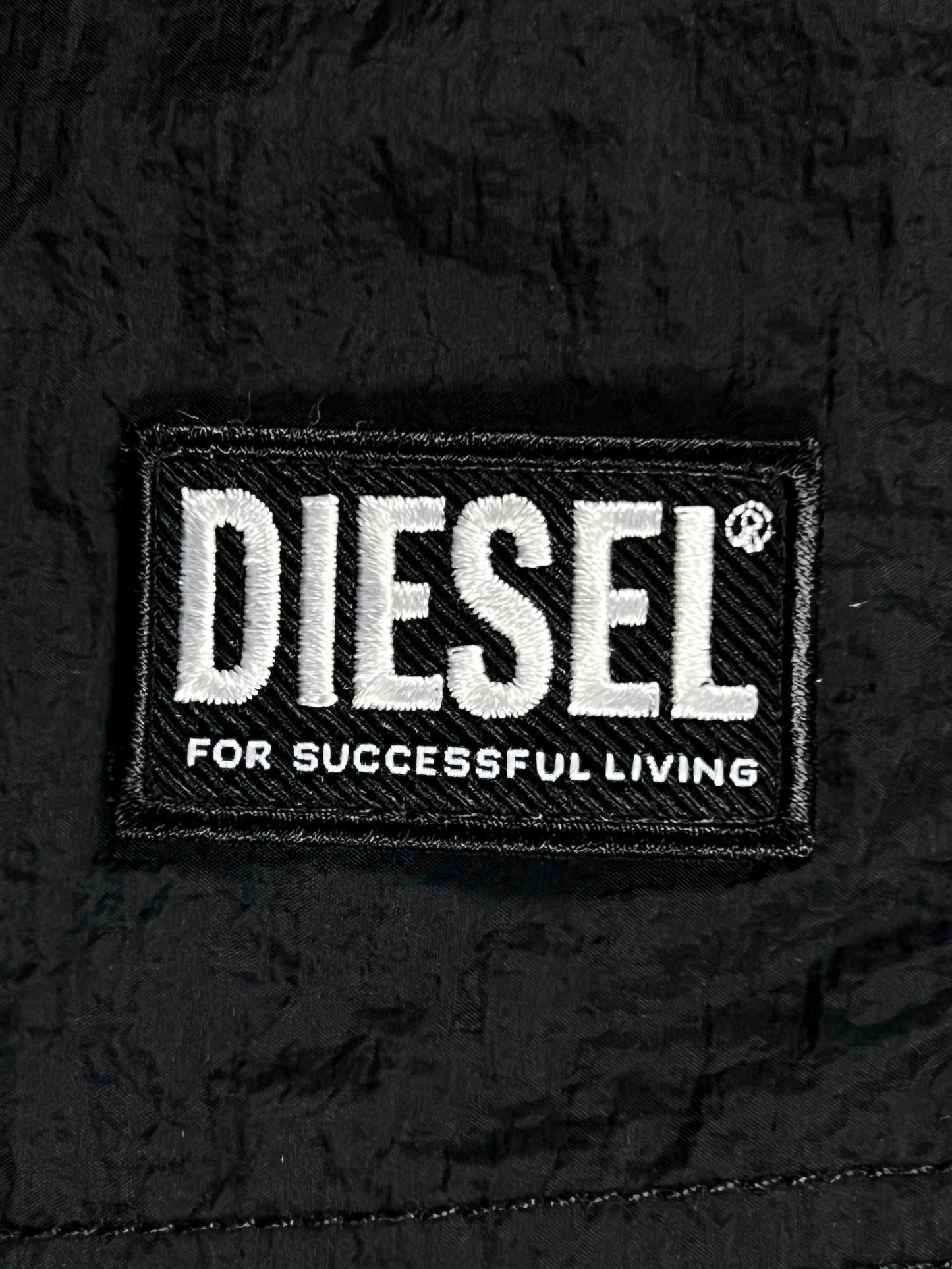 Black DIESEL BMBX-RIO-41CM-PARACHUTE SHORT BLACK label with white embroidered text "diesel" and the slogan "for successful living" on a recycled fabric background.