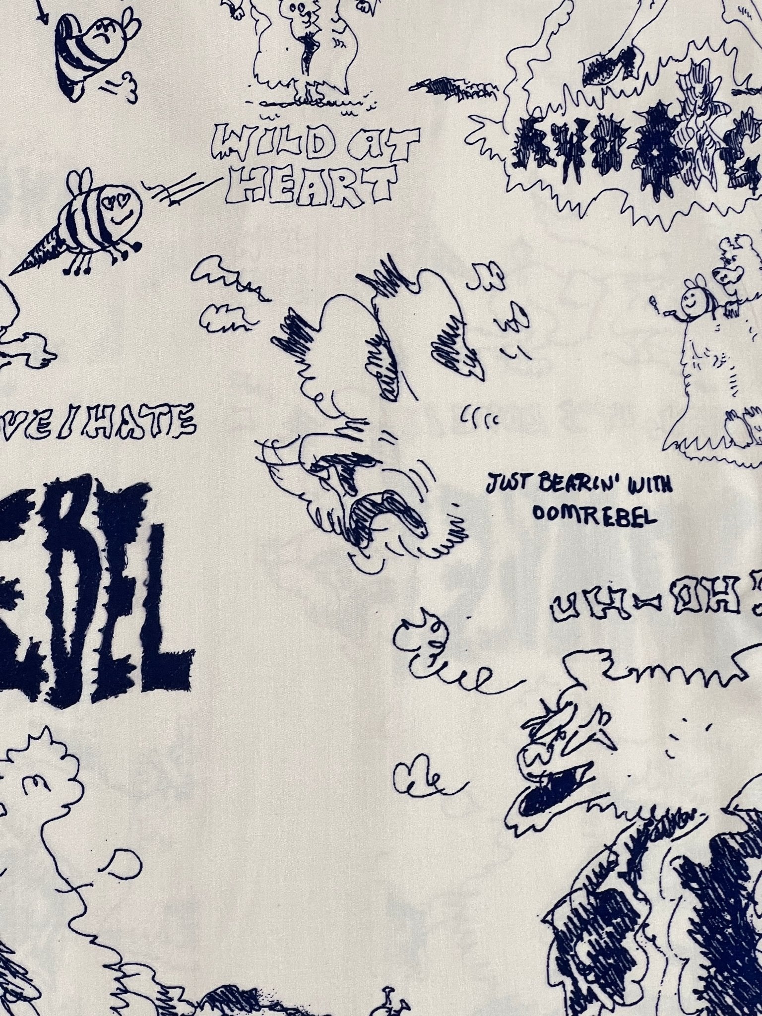 This short sleeve shirt, crafted by DOM REBEL, showcases a whimsical design with black doodles of animals, trees, and playful phrases like "Wild at Heart" and "Just Bearin' With Domrebel." The crisp white background enhances the delightful print. Made from Rayon and Tencel, this fabric is similar to your beloved Domrebel Bearing Camp Collar Shirt Beige.