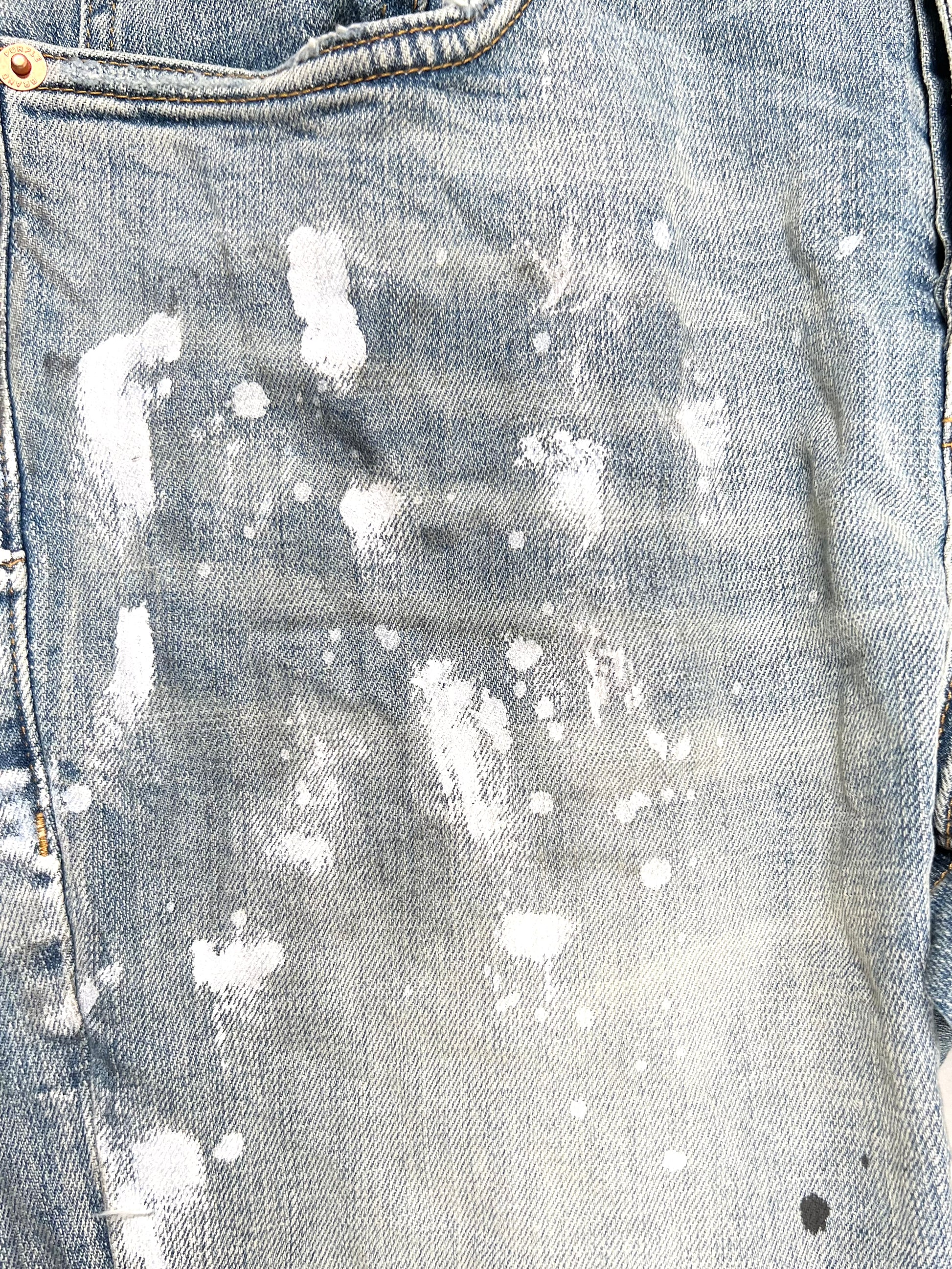 Close-up of Purple Brand Jeans P001-LIA in light indigo, showcasing white paint splatters on the denim fabric and a fashionably worn appearance that echoes PURPLE BRAND's iconic ripped jeans style.