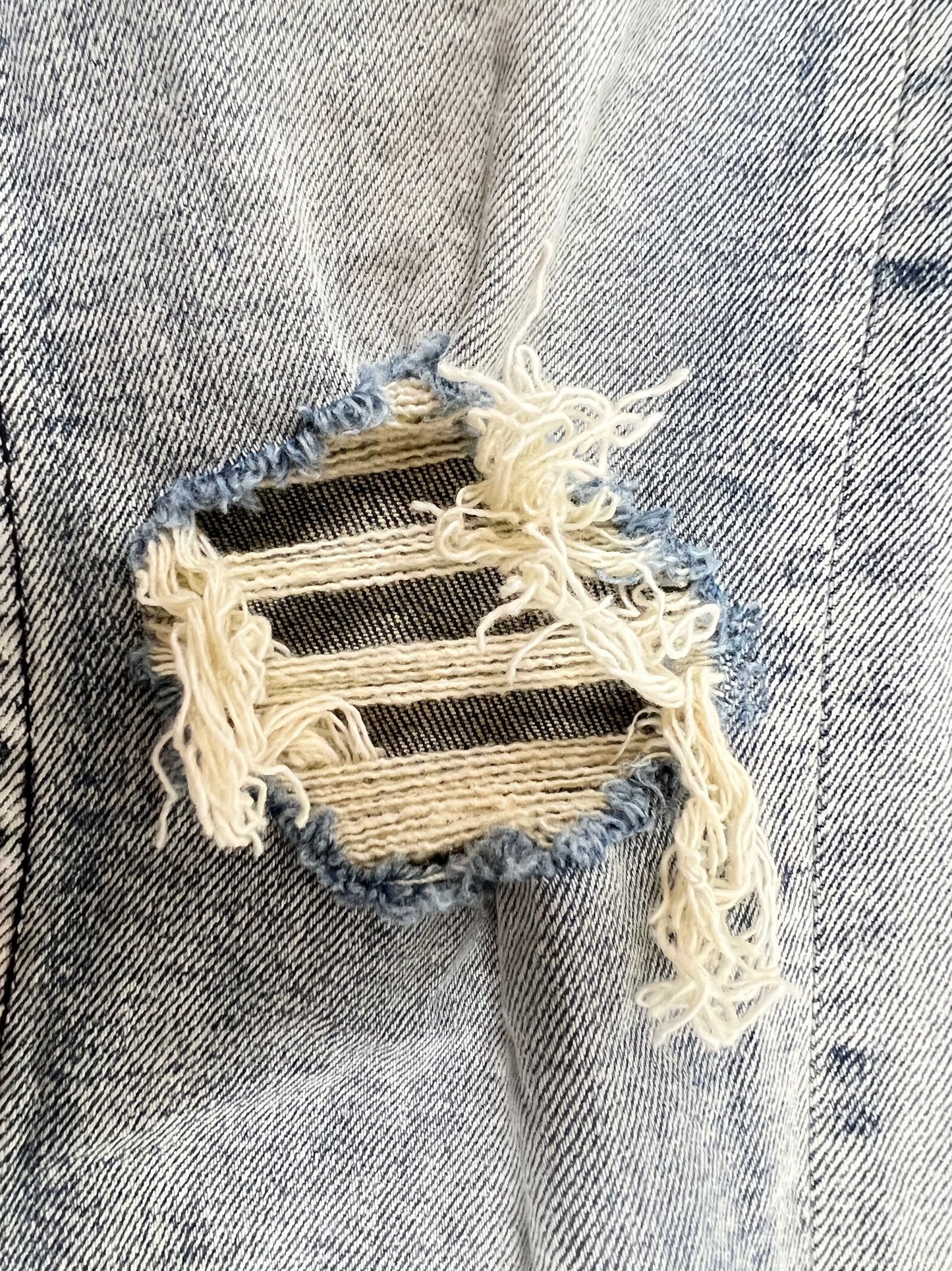 A close up of a light blue, ripped hole in a Ksubi Van Winkle Round Three denim jacket.