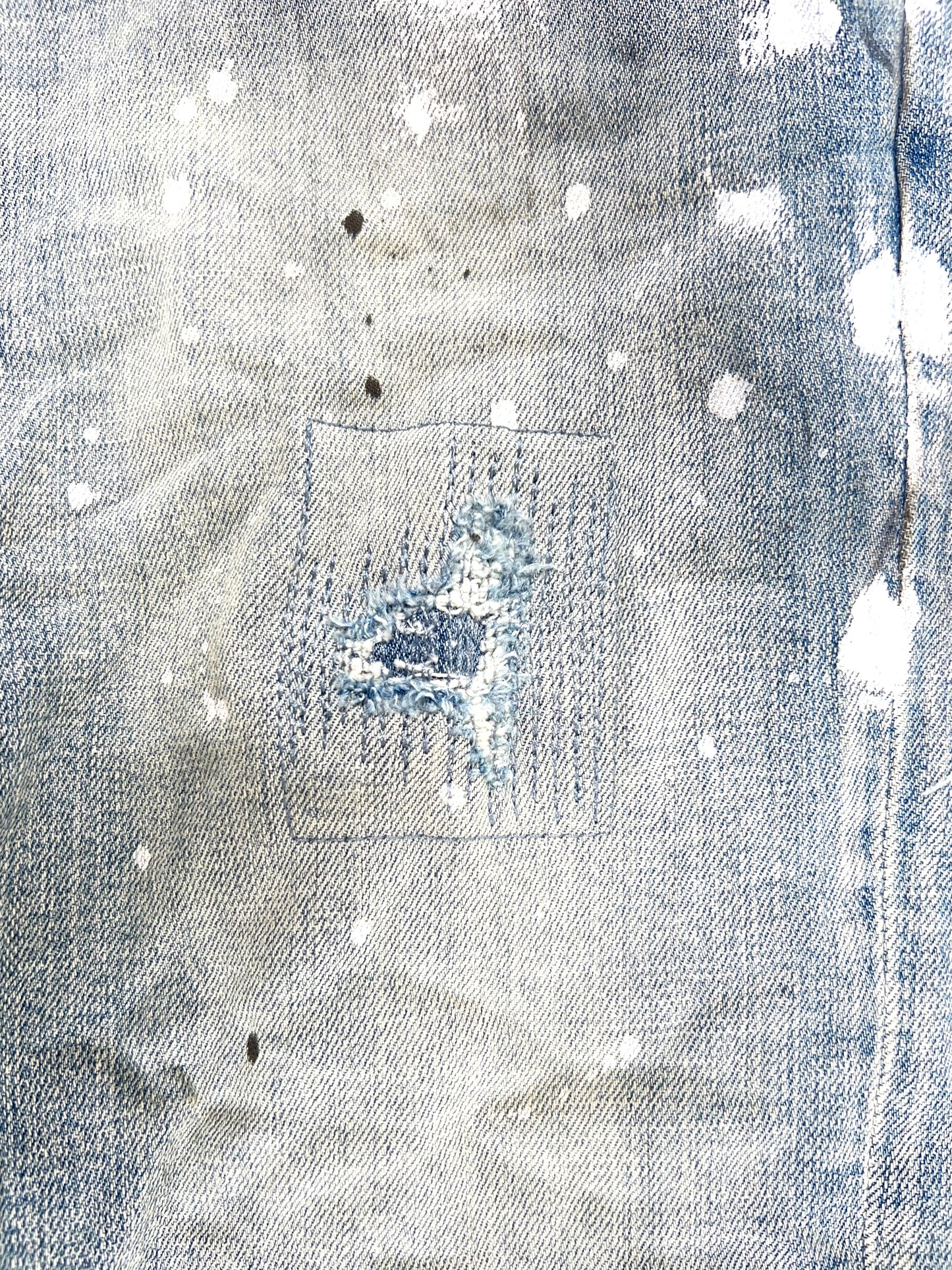 A close-up of a ripped denim jacket with paint on it. 
Product Name: PURPLE BRAND JEANS P001-LIA LIGHT INDIGO PAINT BLOWOUT 
Brand Name: PURPLE BRAND