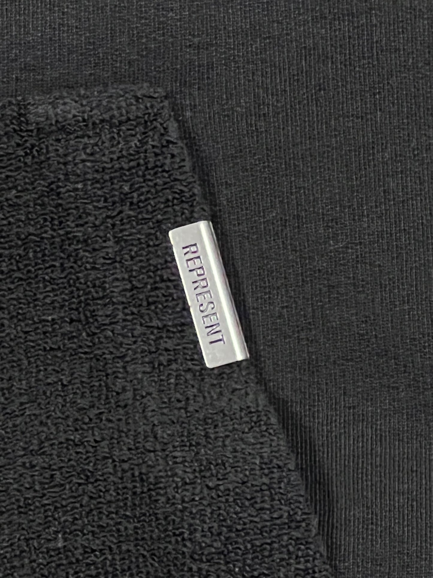 A close up of a REPRESENT M04216 INVERSE HOODIE OFF BLACK with a label on it.