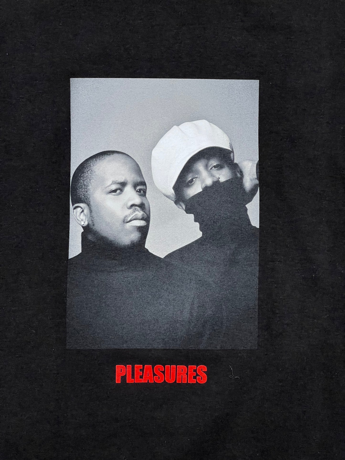 A PLEASURES black t-shirt adorned with a picture of two men discussing their vocabulary pleasures.