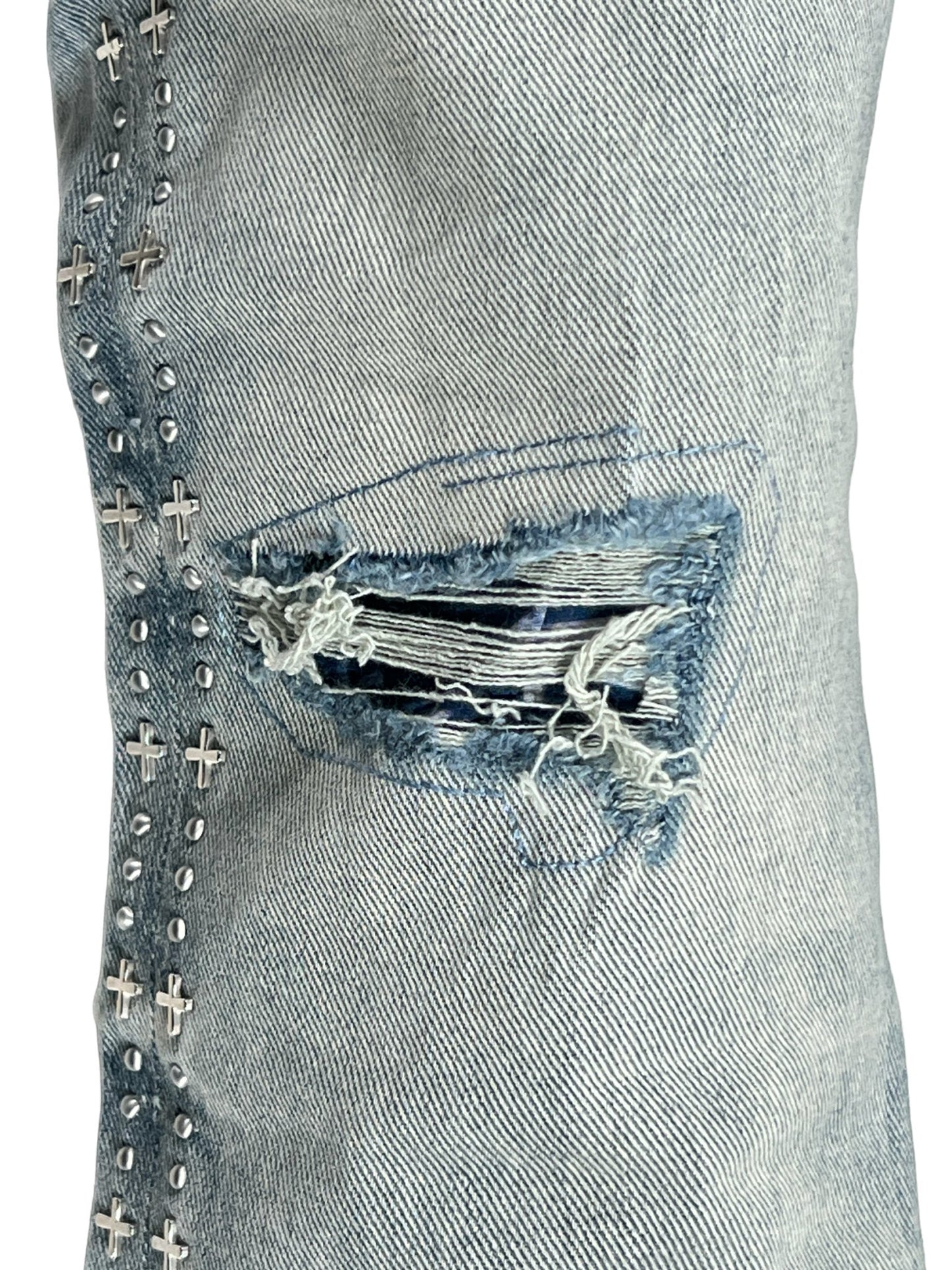 Close-up of a distressed KSUBI BRONKO DYANAMITE METAL DENIM fabric with a ripped patch and metal stud embellishments.