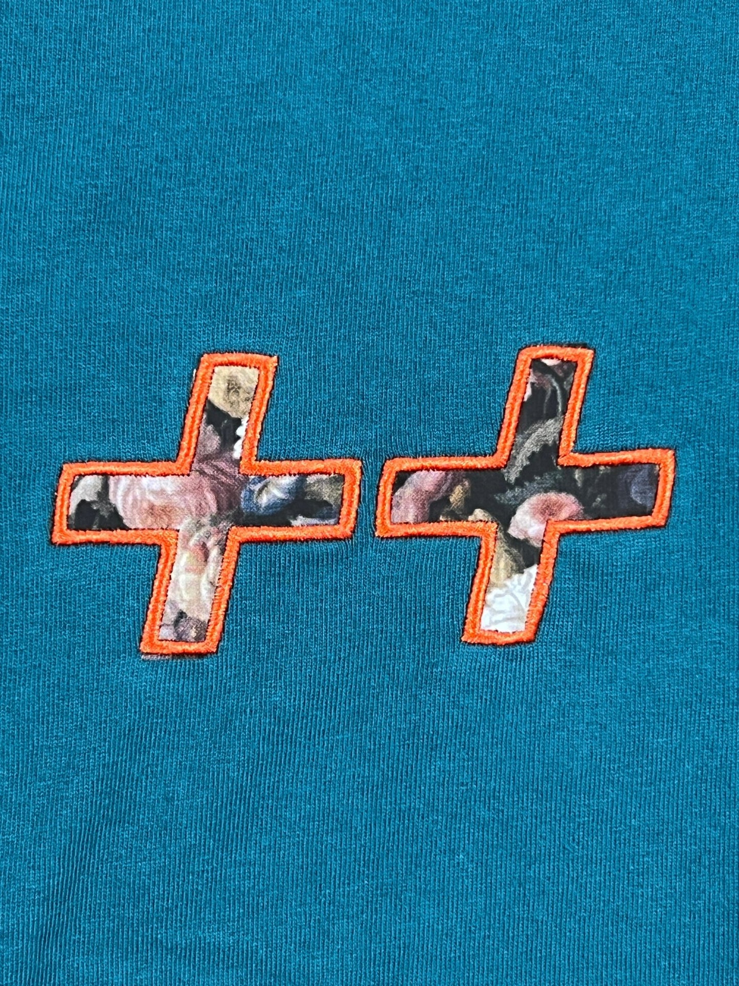 A KSUBI ECOLOGY BIGGIE SS TEE TEAL BLUE with two embroidered crosses on it.