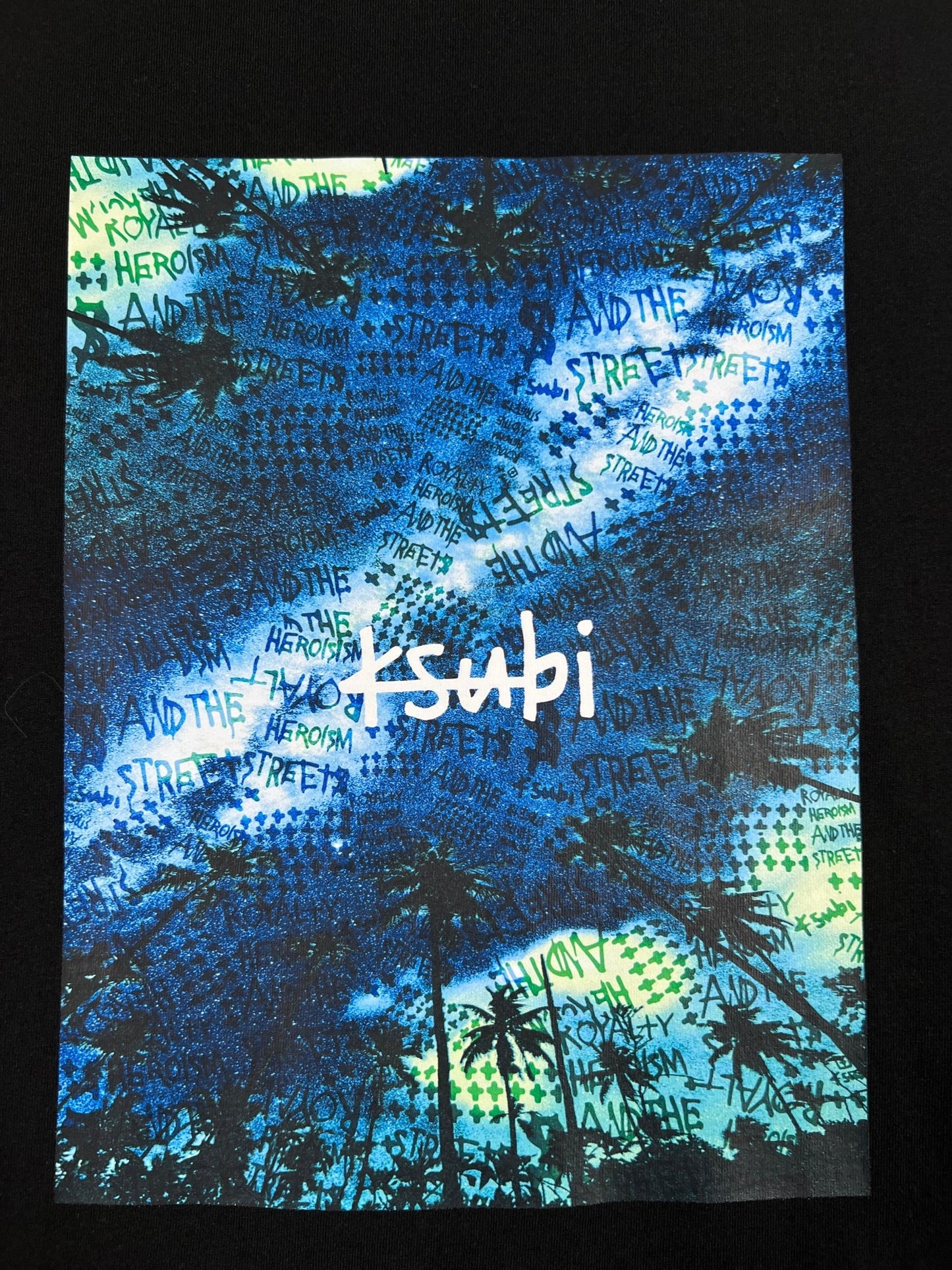 The KSUBI SPACE PALM BIGGIE SS TEE JET BLACK from KSUBI is a graphic T-shirt on a black background featuring blue and green patterns with overlaid text in black. The central white text reads "KSUBI." Crafted from 100% cotton, it exudes both style and comfort.