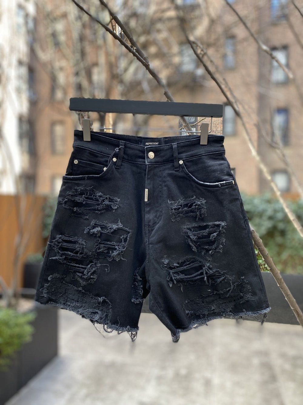 A pair of REPRESENT M07062 SHREDDED DENIM SHORTS BLACK hanging on a tree.