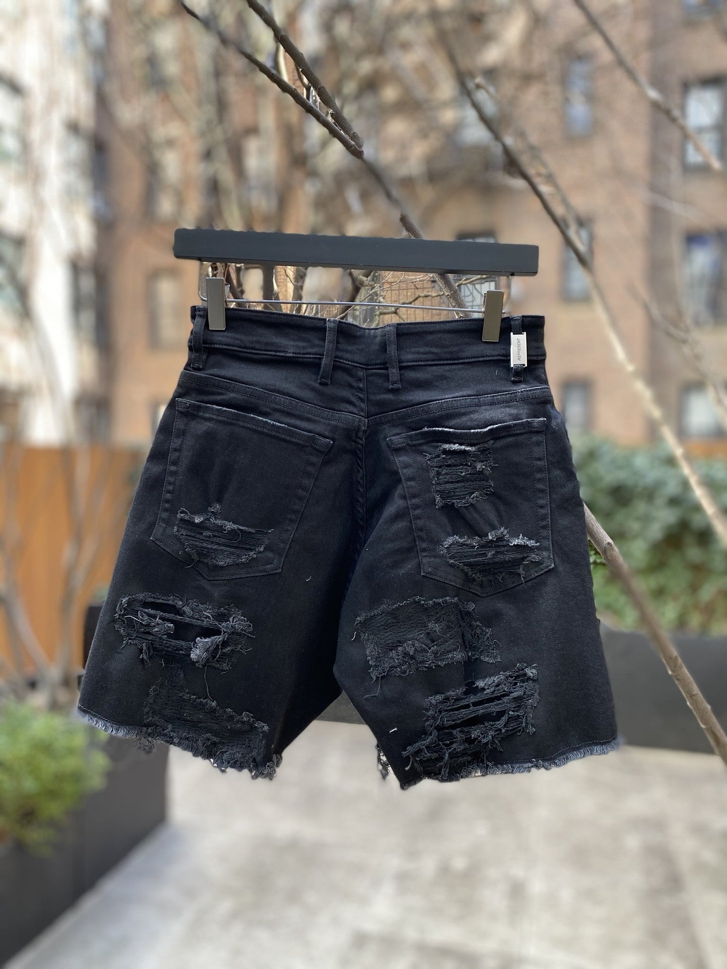 A pair of REPRESENT's M07062 SHREDDED DENIM SHORTS BLACK hanging on a tree.