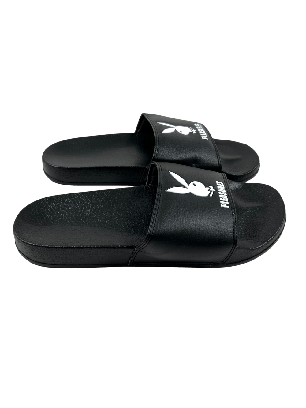 A pair of black PLEASURES PLAYBOY slides with a white logo.