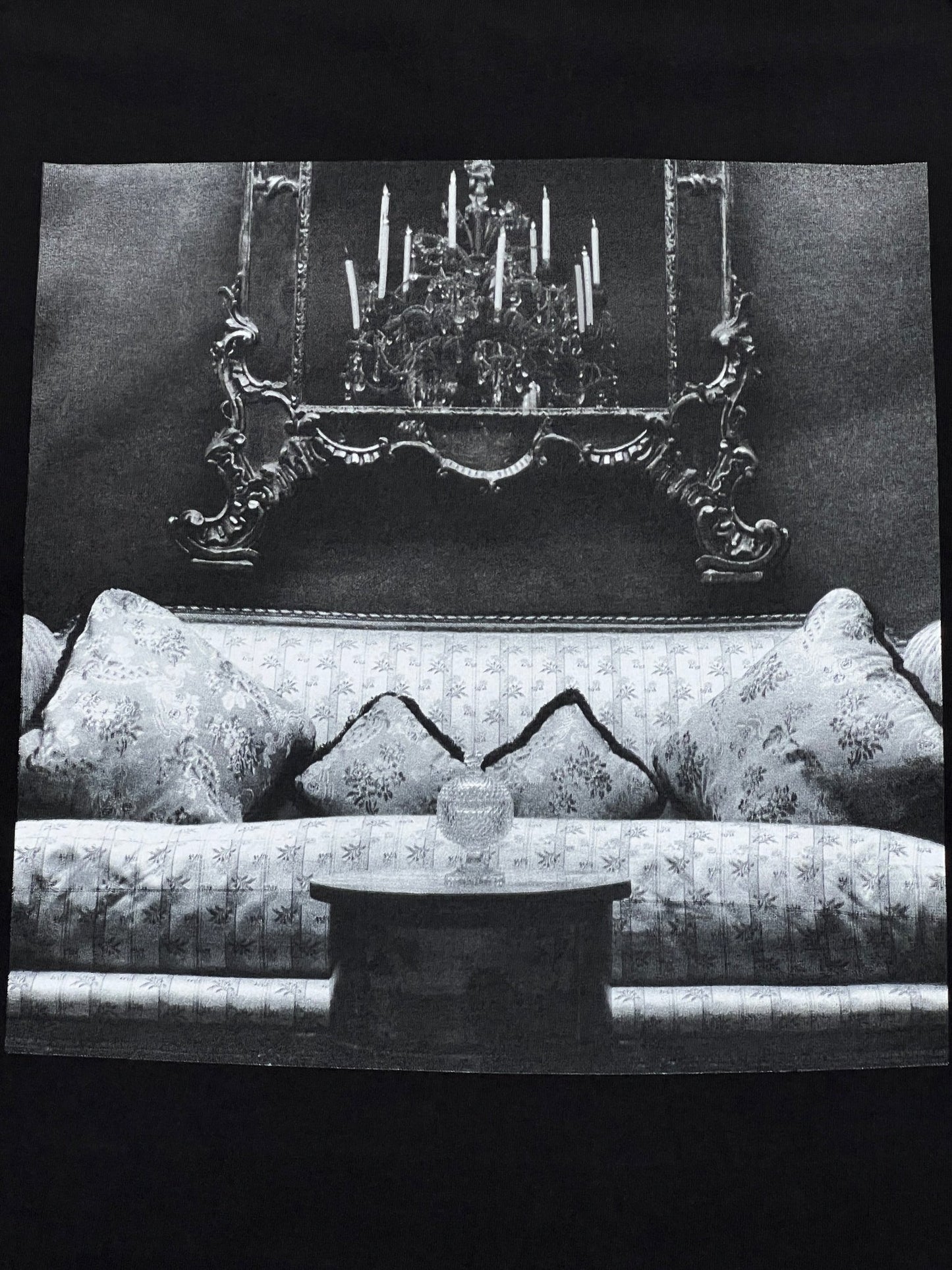 A PLEASURES black t-shirt with an image of a couch and a chandelier.