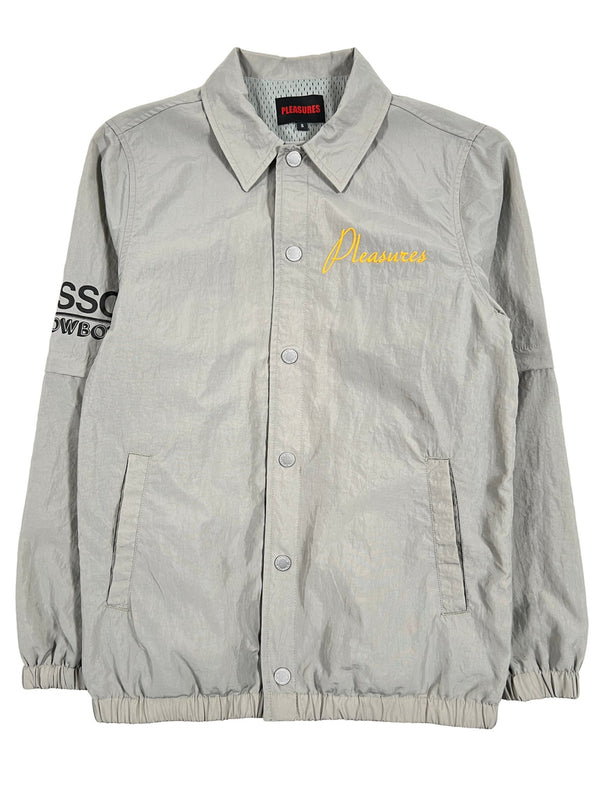 A grey Polyester jacket with the PLEASURES GYPSY COACH JACKET MATCHA embroidered logo detail on it.