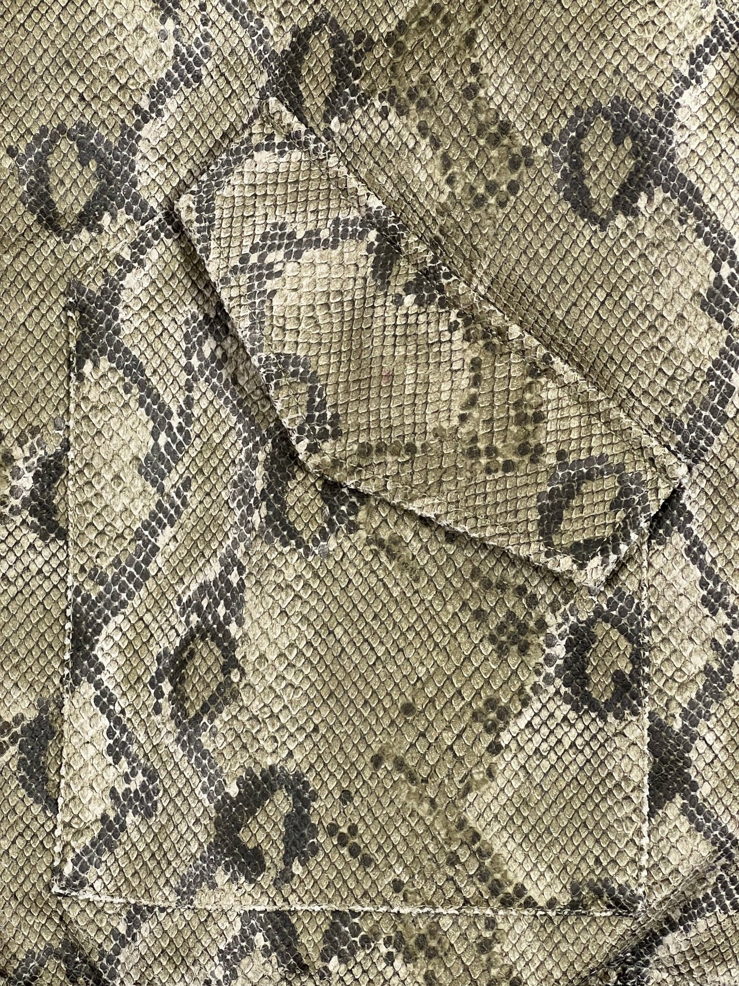 A close up of a PLEASURES python skin pocket with quilted lining.
